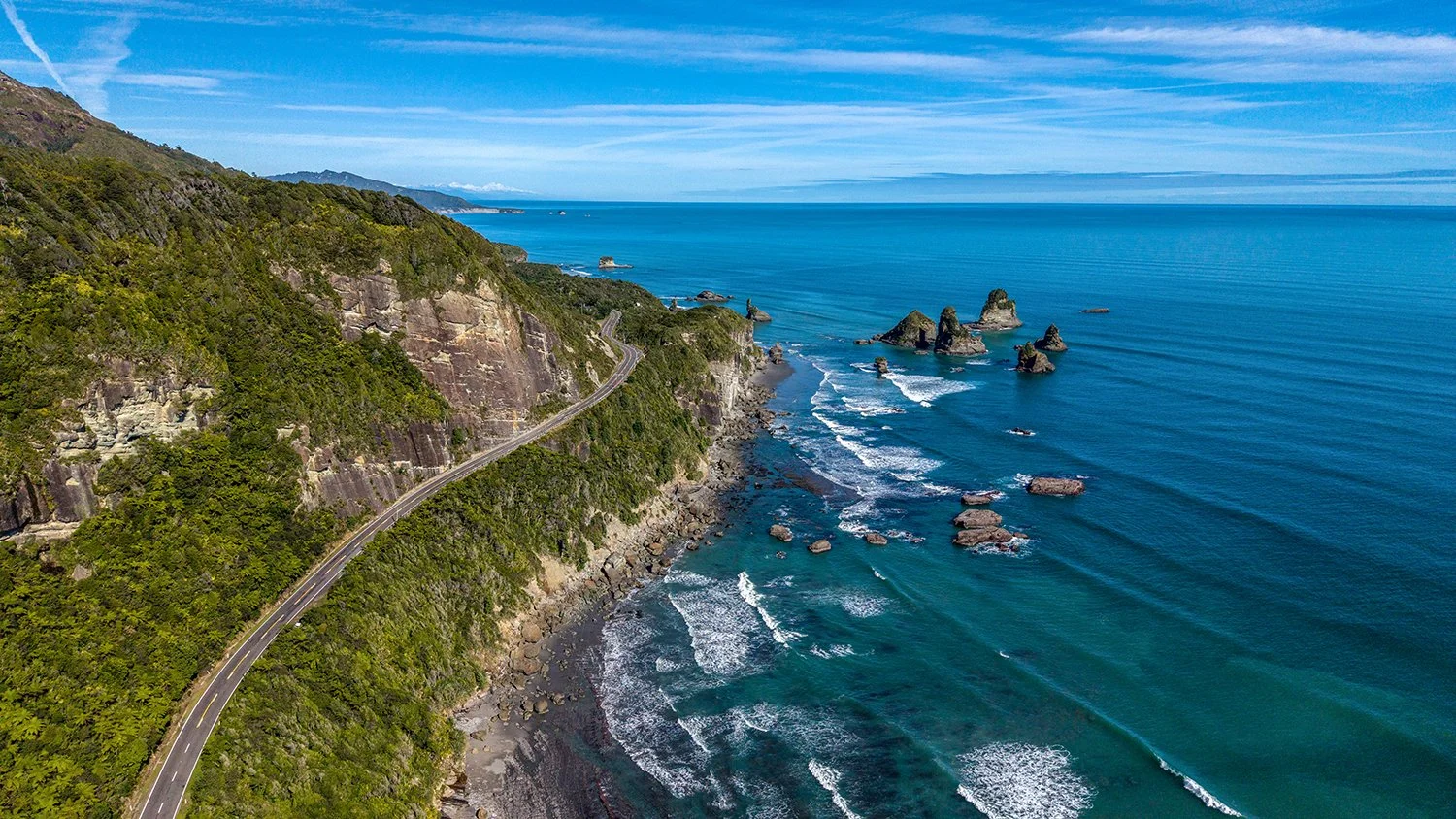 Coastal road winding beside sea stacks and ocean on the West Coast.