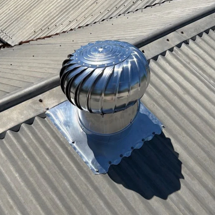 A metal turbine roof vent installed on a corrugated metal roof, casting a shadow on the roof surface.
