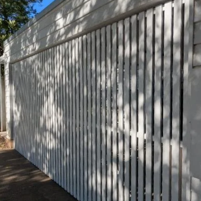 A white wooden fence casting shadows from nearby trees on a sunny day.