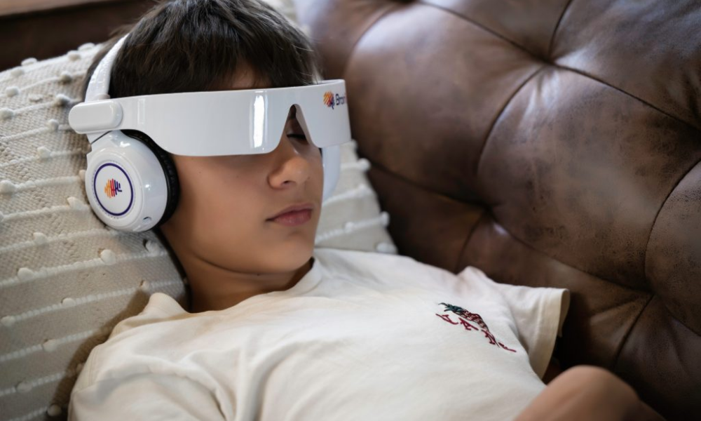 Young boy lying on a couch, wearing a virtual reality headset and headphones, resting with closed eyes.