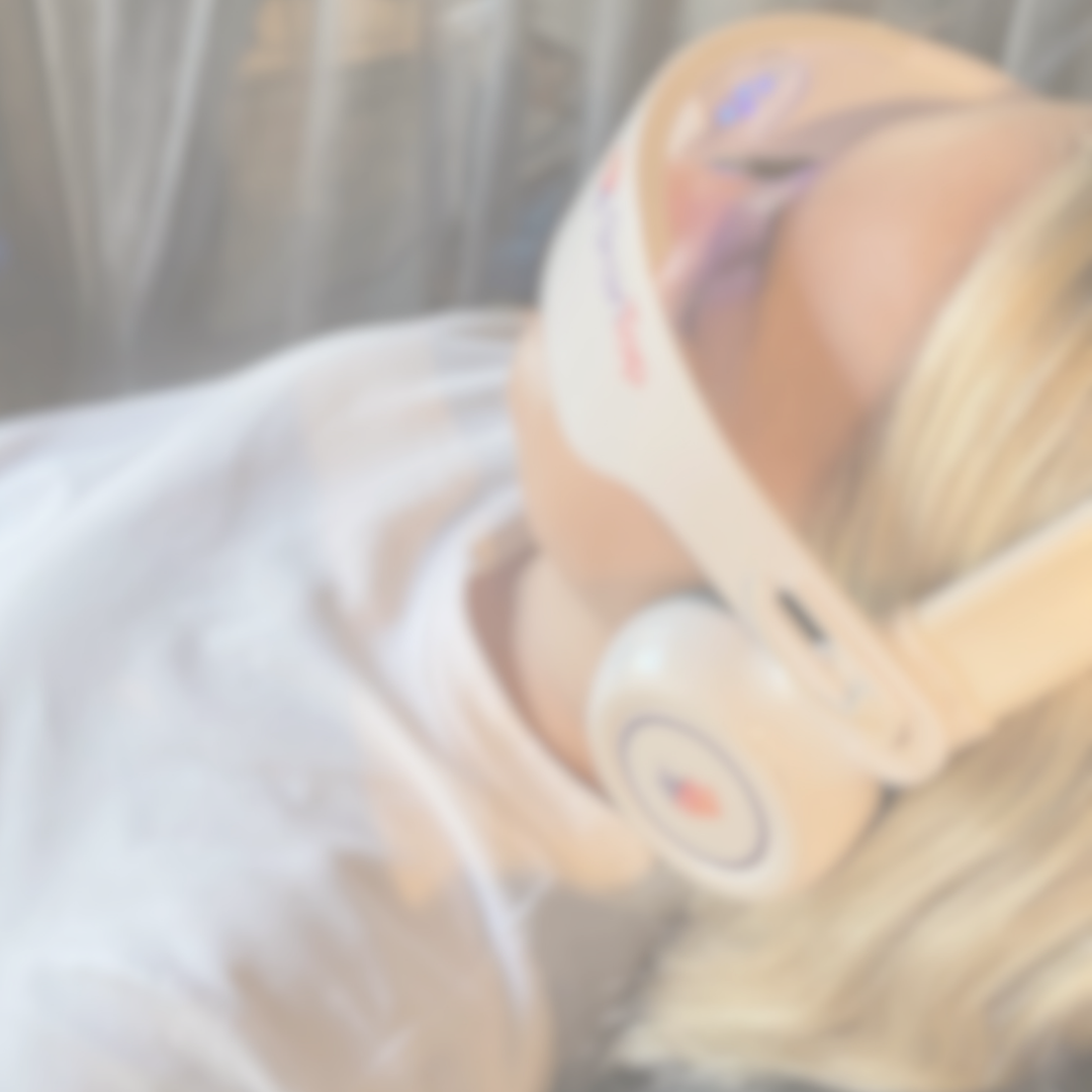 A person lying on a hospital bed wearing a protective face mask and a medical gown, with a medical device on their head.