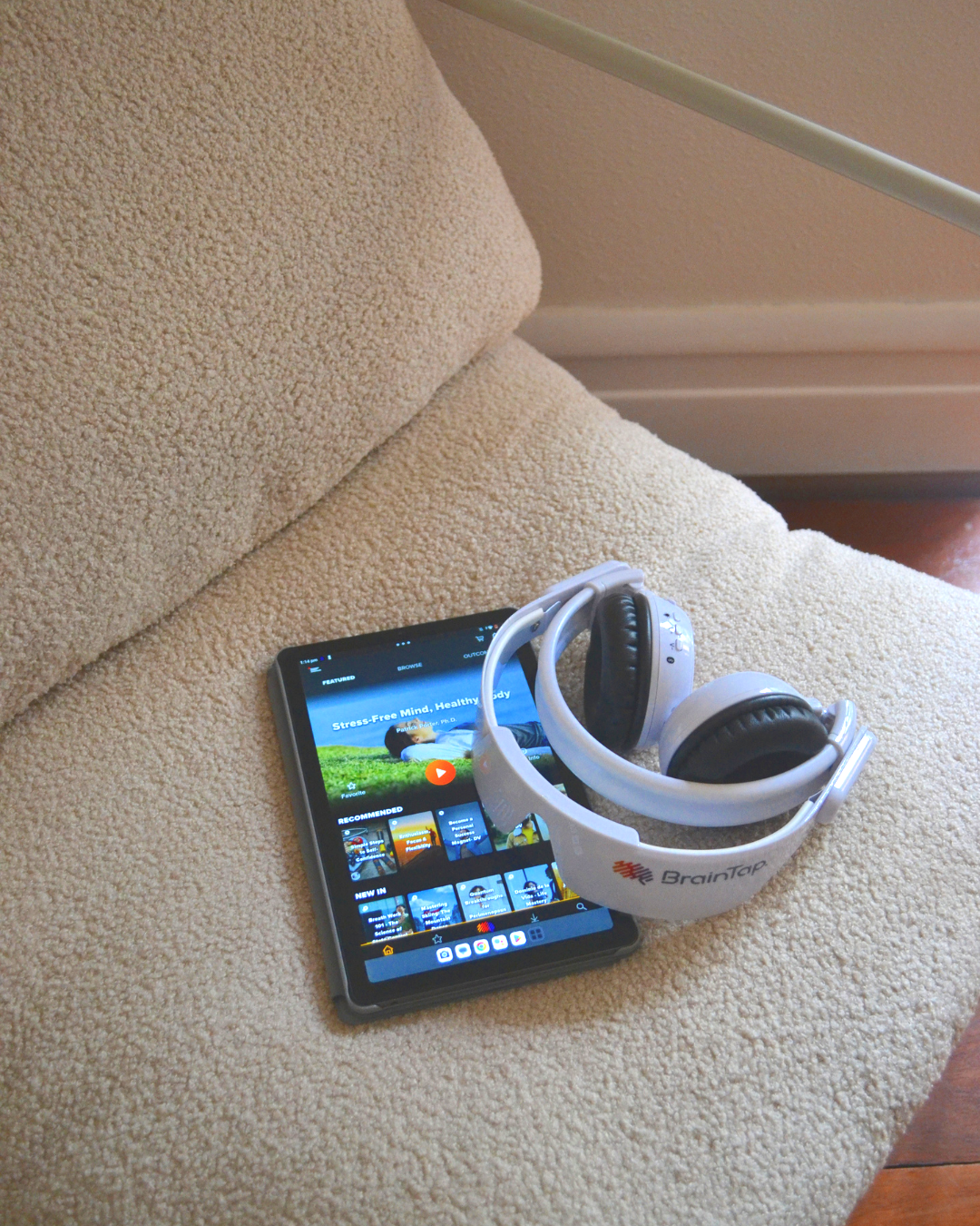 A smartphone and a pair of white headphones on a beige upholstered chair.