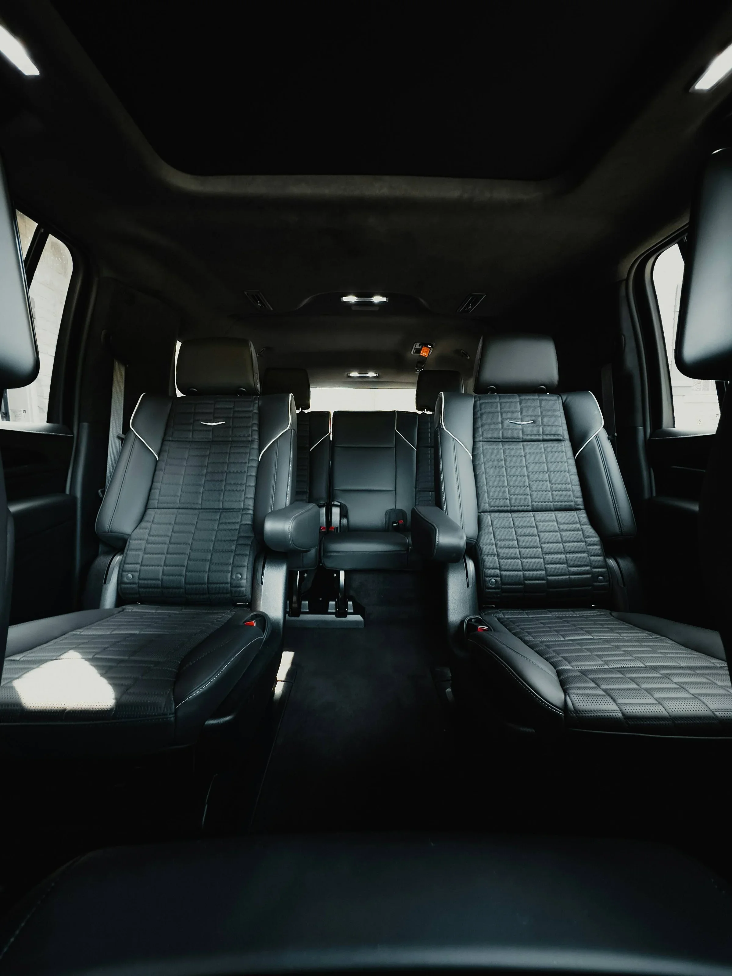Interior of a luxury vehicle with black leather seats, equipped with quilted stitching, armrests, and headrests, viewed from the back seat looking forward.
