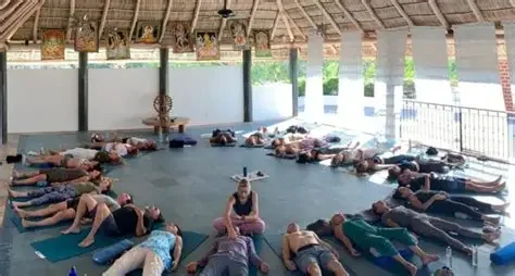 People practicing yoga on mats underneath a covered outdoor area.