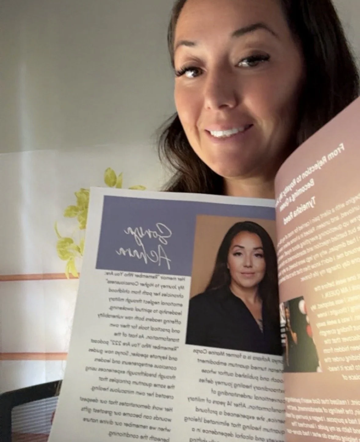 Woman with long dark hair smiling while holding a magazine open to a page featuring her photograph and an autograph.