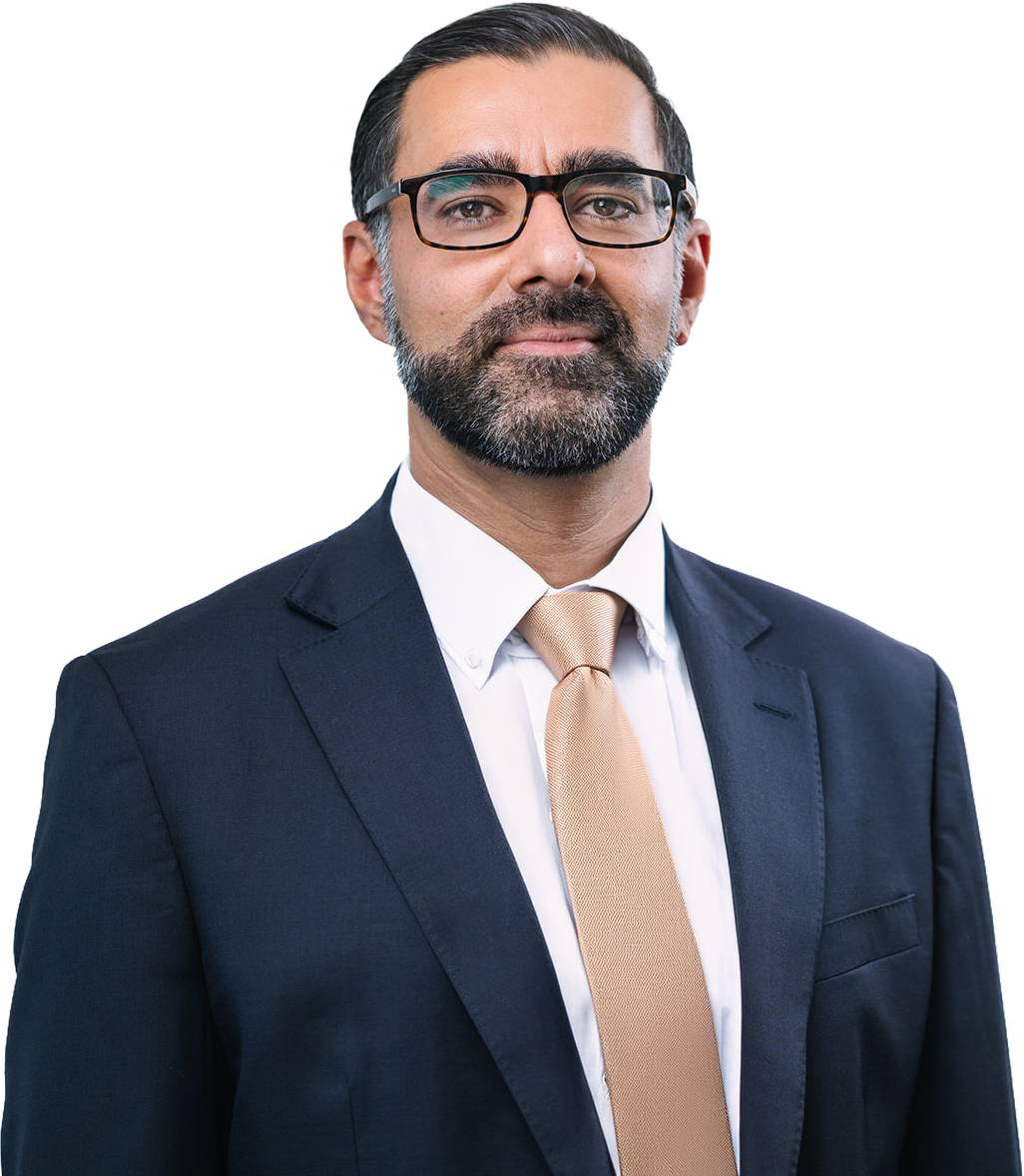 A professional man with dark hair, beard, and glasses wearing a navy blue suit, white shirt, and beige tie.