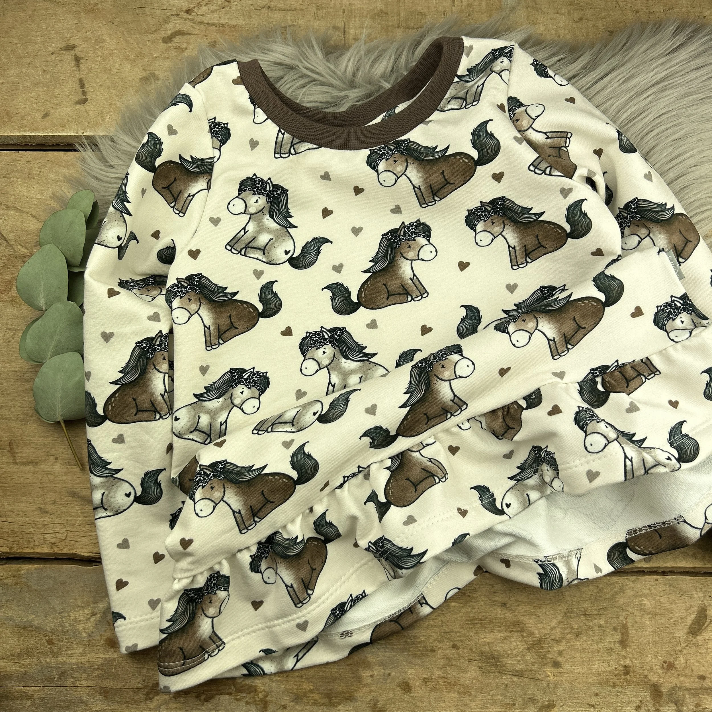 Cutie-Shirt Gr. 62-146 (Einzelgrößen).

Der Schnitt ist im Vokuhila-Stil und leicht ausgestellt. Mit langen oder kurzen Ärmeln. Optional mit Volantsaum / Volantärmeln. An Armen und Bauch gesäumt. Der Halsausschnitt wird mit einem Bündchen versehen. O