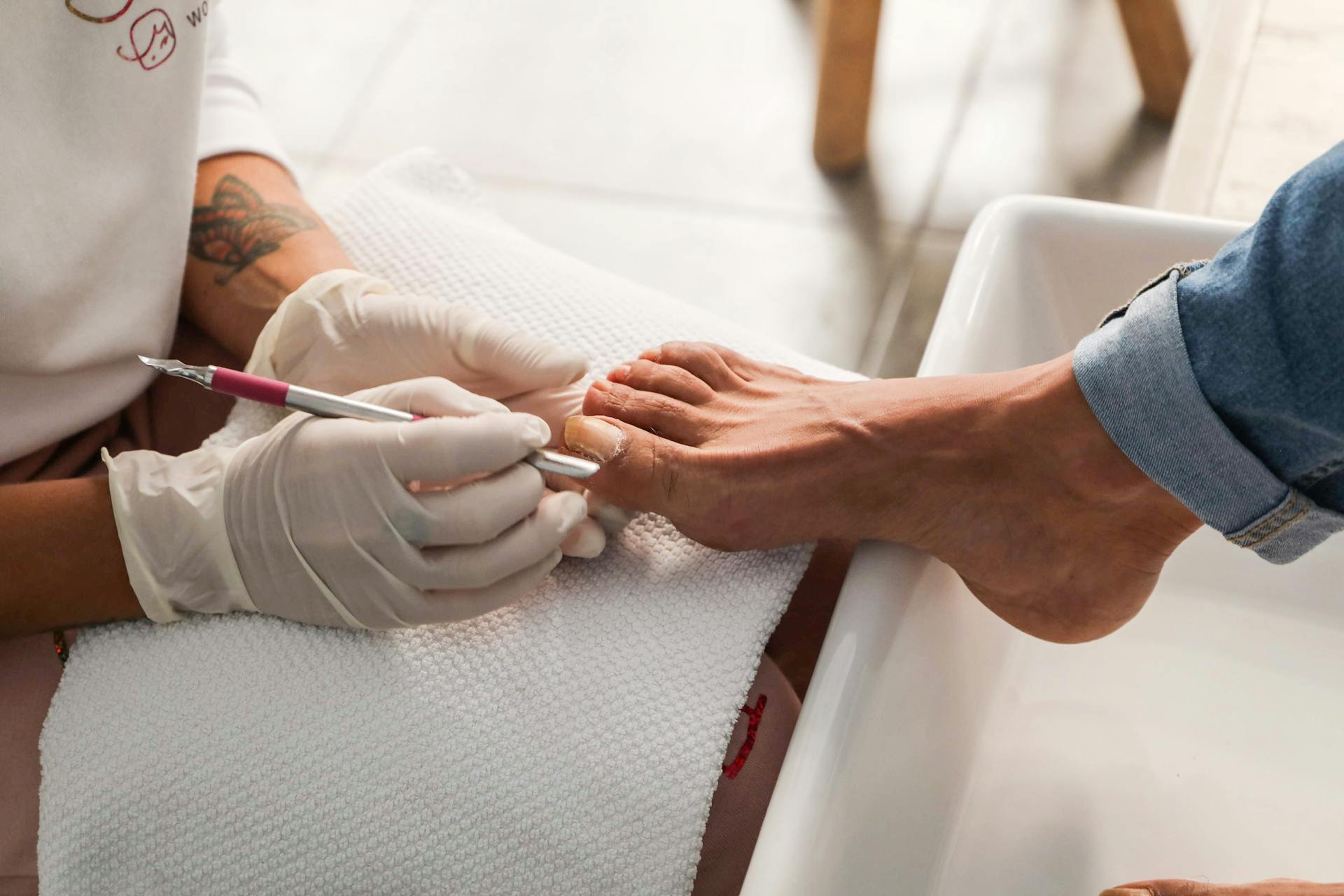 Tattooed person receiving a manicure at a salon, with a nail technician applying nail polish or a decorative design to their fingernail.