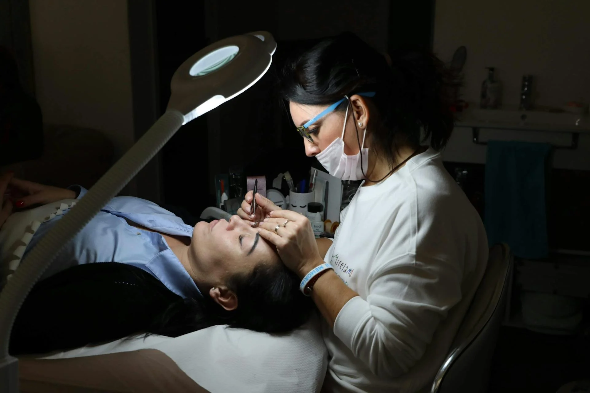 A woman receiving a cosmetic or medical facial treatment from a professional in a dimly lit clinic or spa setting.
