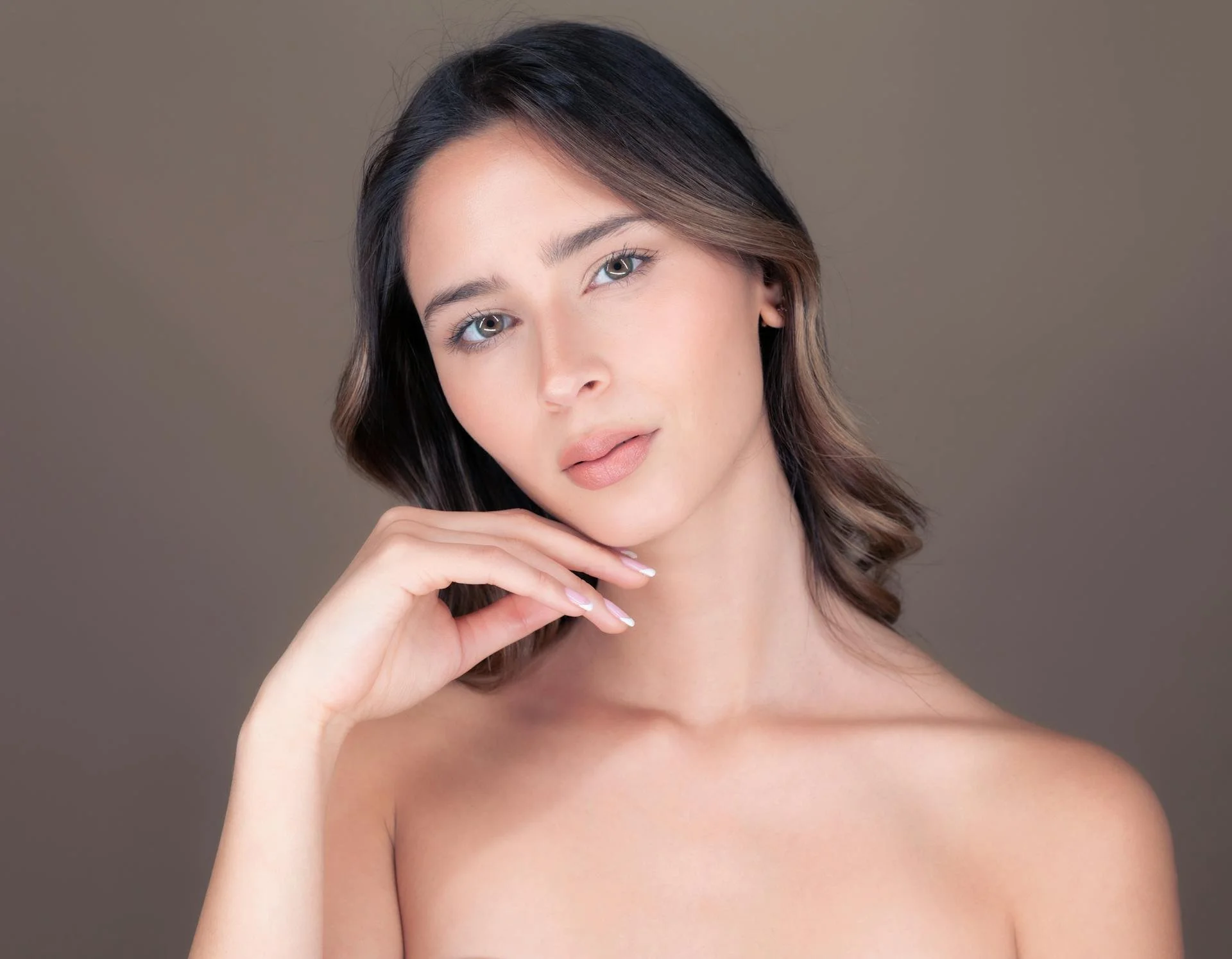 A woman with shoulder-length brown hair and blue eyes posing against a plain background.