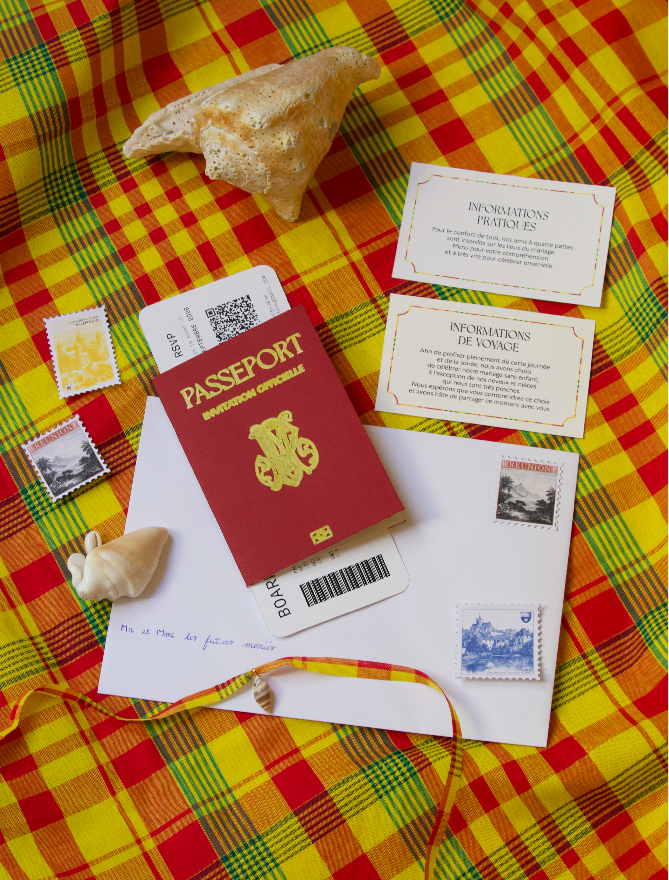 Une table recouverte d'une nappe à carreaux rouge, jaune, vert et orange. Sur la nappe, il y a une coquille de mollusque, plusieurs papiers, une pièce de monnaie, un passeport rouge, un billet de train, et des timbres.