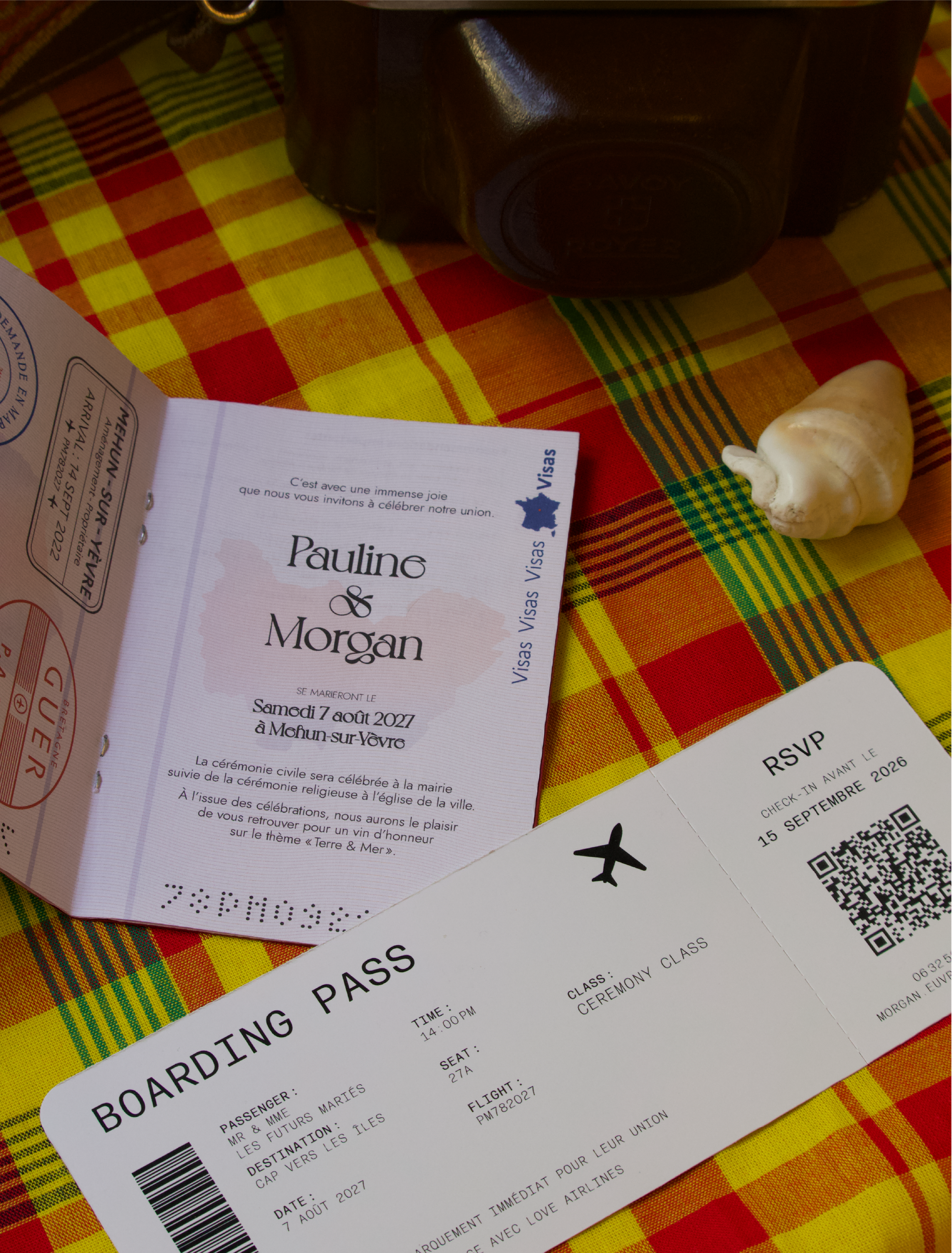 Billet d'avion pour le mariage de Pauline et Morgan le samedi 7 août 2027 à Melun-sur-Yèvre, avec informations sur le vol et le passager, posé sur un tissu à carreaux colorés.