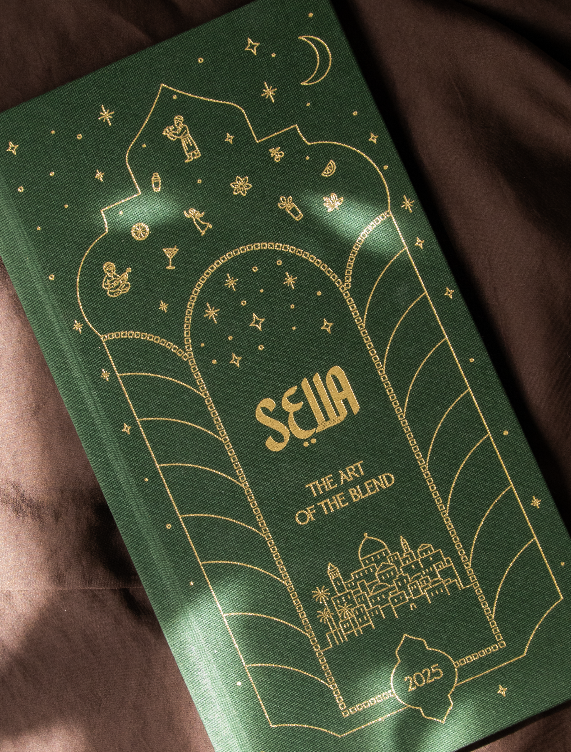 Une boîte verte avec des illustrations dorées représentant des éléments festifs et artistiques, incluant des personnages, des étoiles, une lune, des décorations et la mention '2025'.