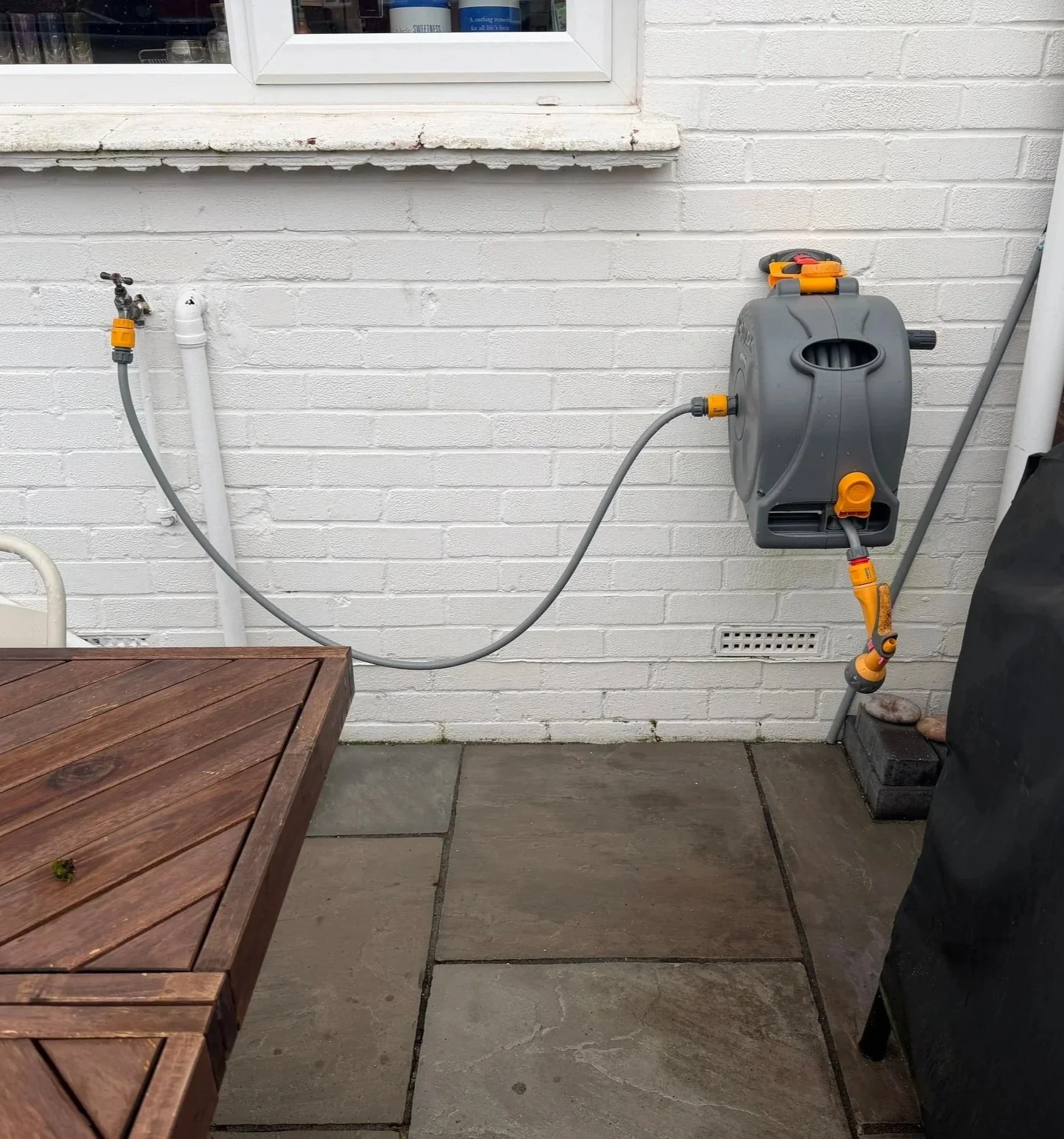 A garden hose reel mounted on a white brick wall with a hose connected to a water spigot.