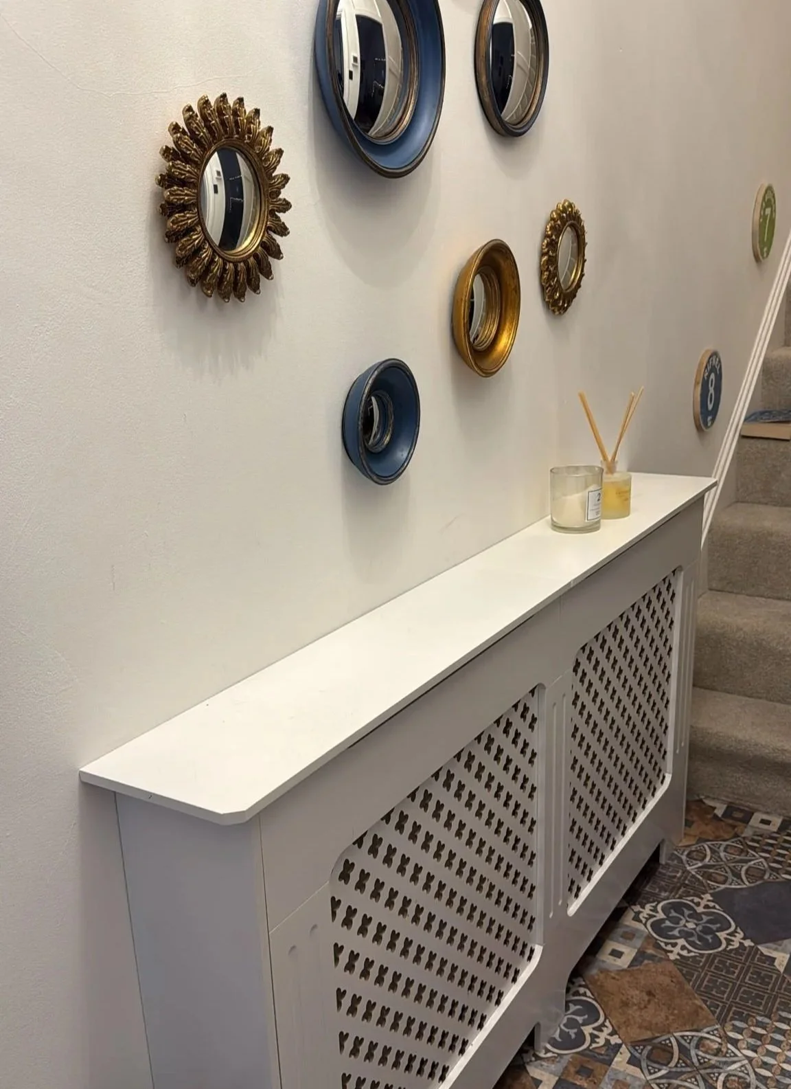 White custom built radiator cover with several wall mounted feature mirrors above