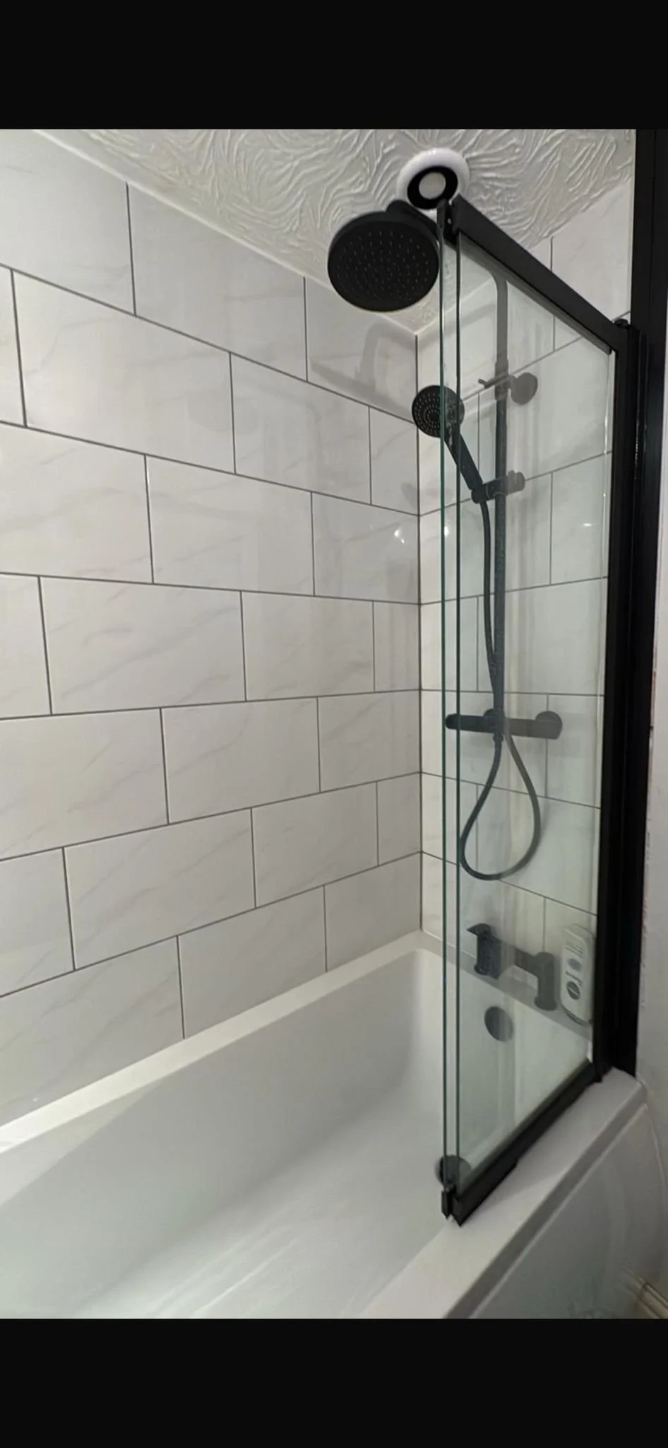 Modern shower with black fixtures, black shower head, handheld shower wand, and a glass shower door.