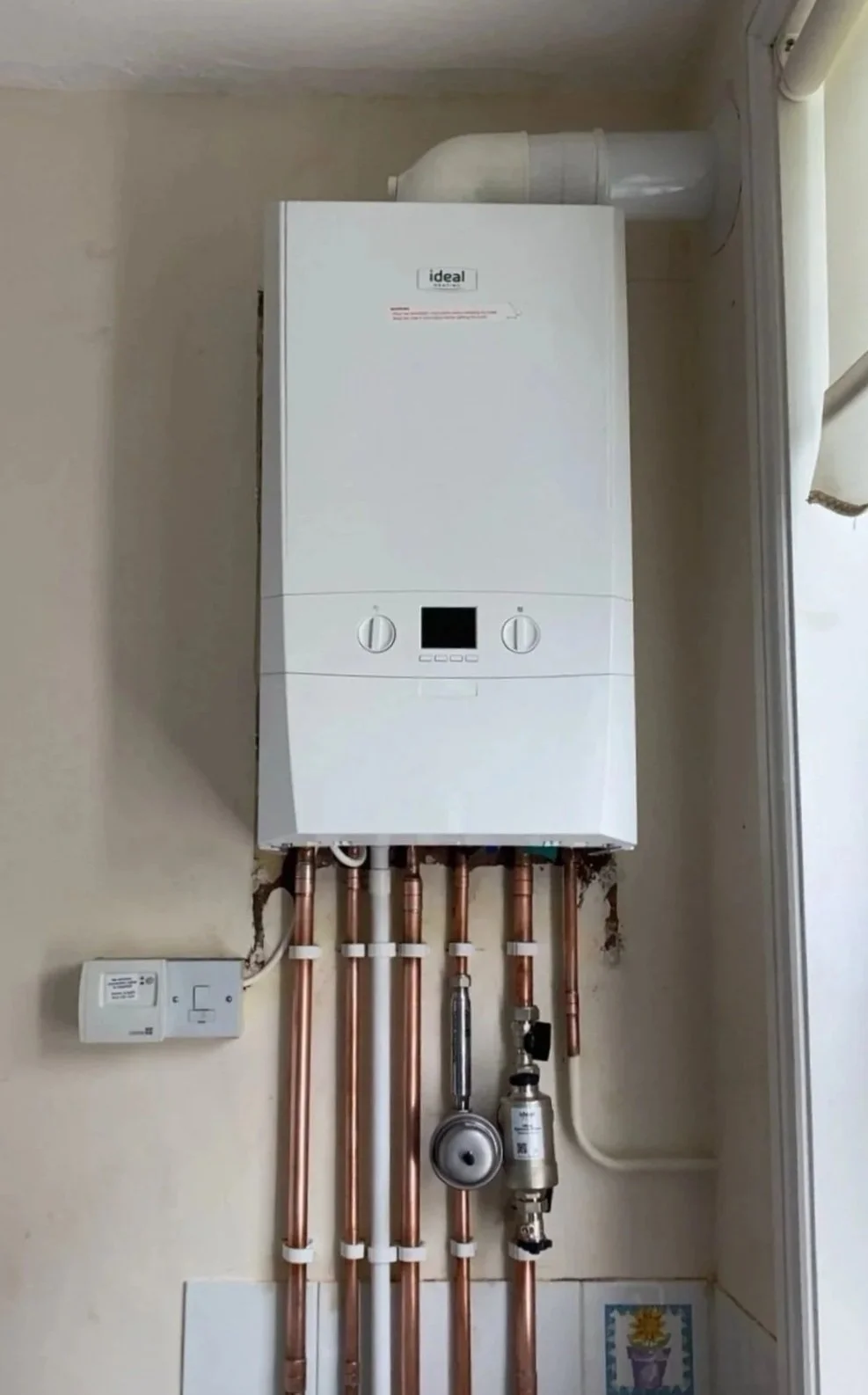 Wall-mounted boiler with copper pipes and controls in a utility room.