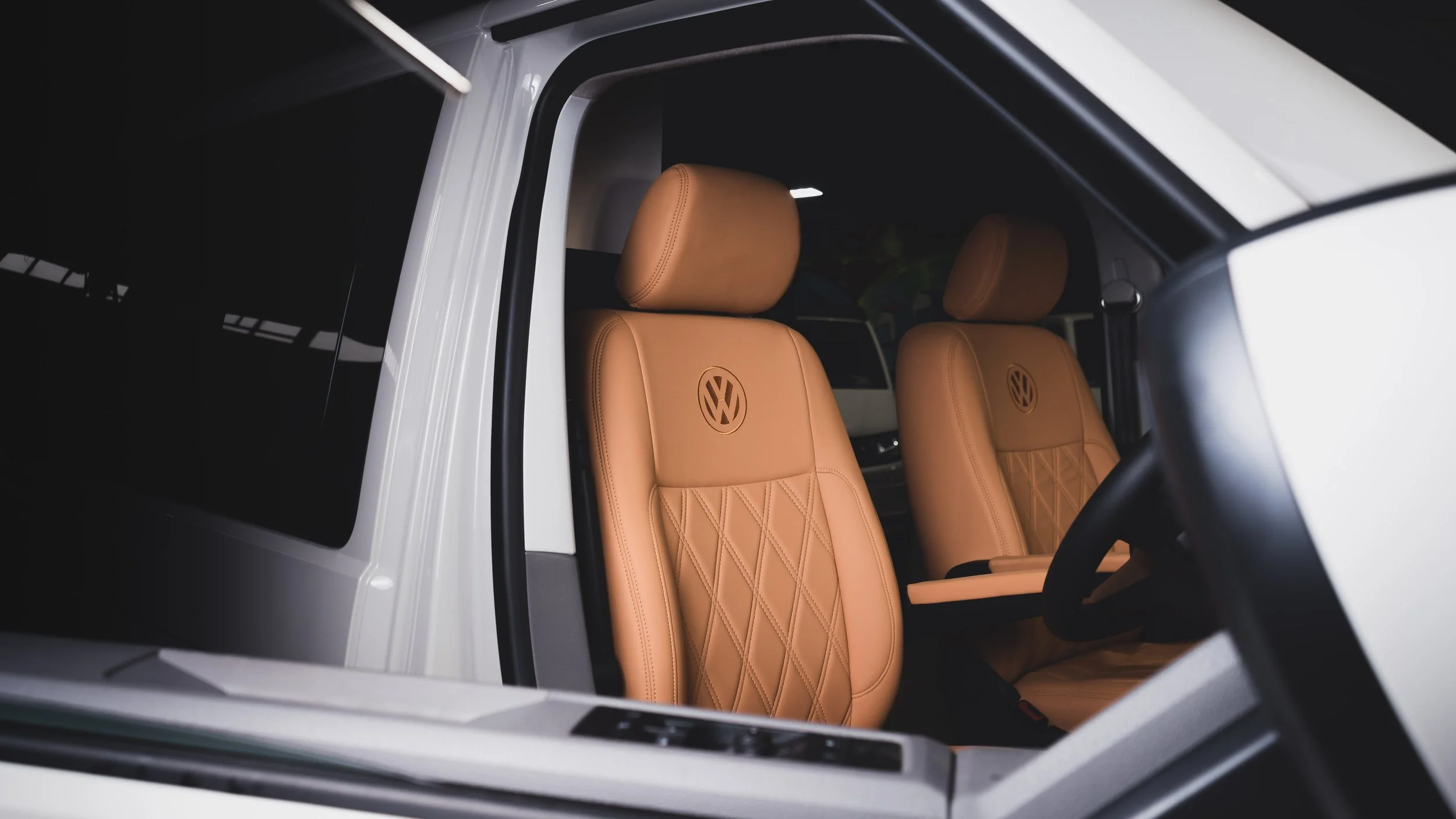 Close-up of the interior of a Volkswagen vehicle with tan leather seats embossed with the VW logo, showing the front seats and part of the steering wheel.