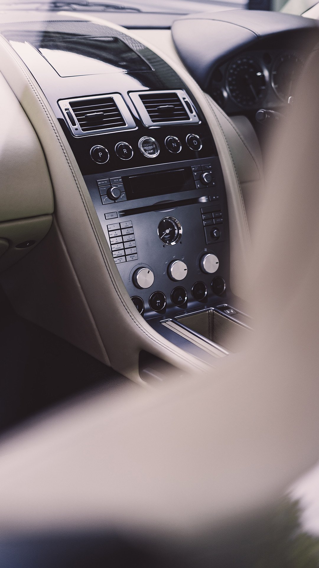 The interior of a luxury car with a beige dashboard, black center console with various controls and knobs, and gear shift area.