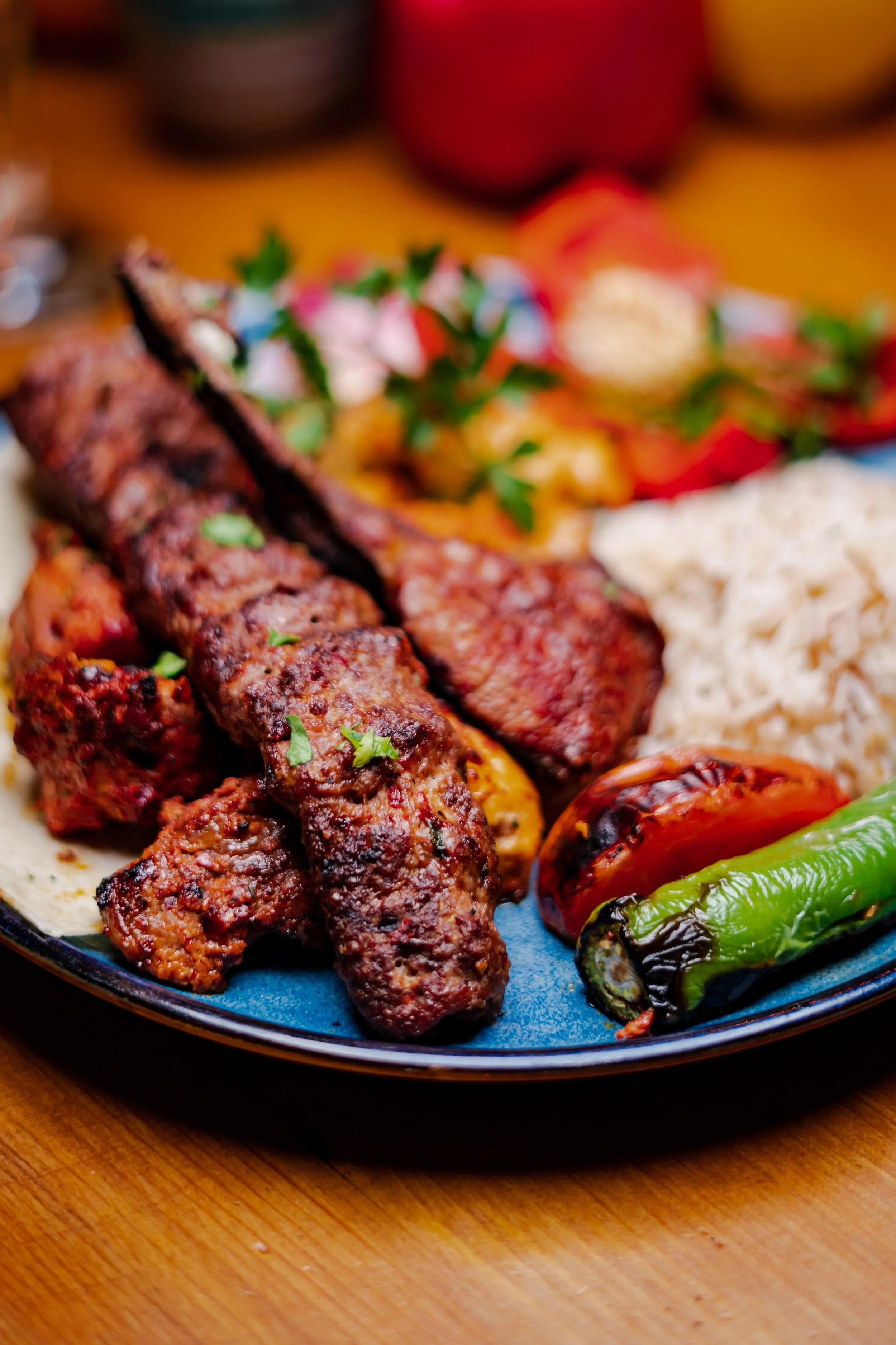 Plate of grilled meat, rice, grilled tomato, and a green chili pepper on a wooden table.