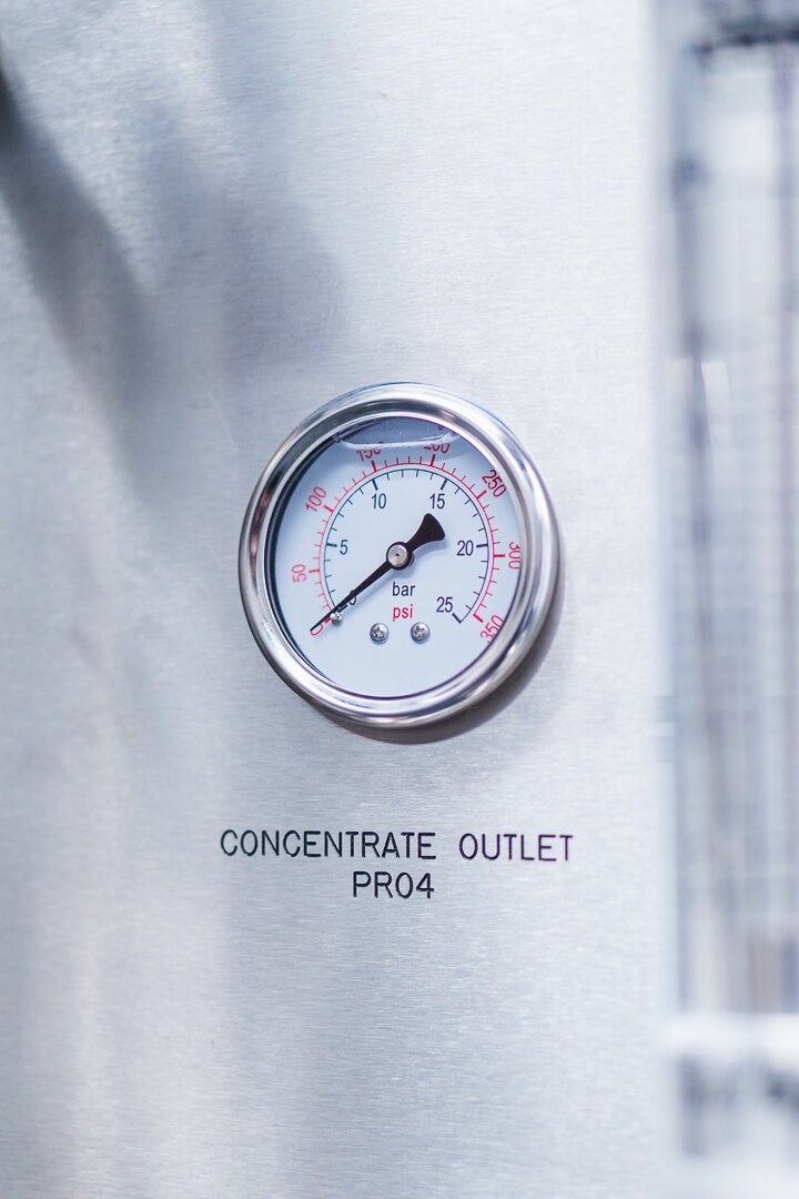 Pressure gauge indicating about 15 psi on a stainless steel surface labeled 'Concentrate Outlet PRO4'.
