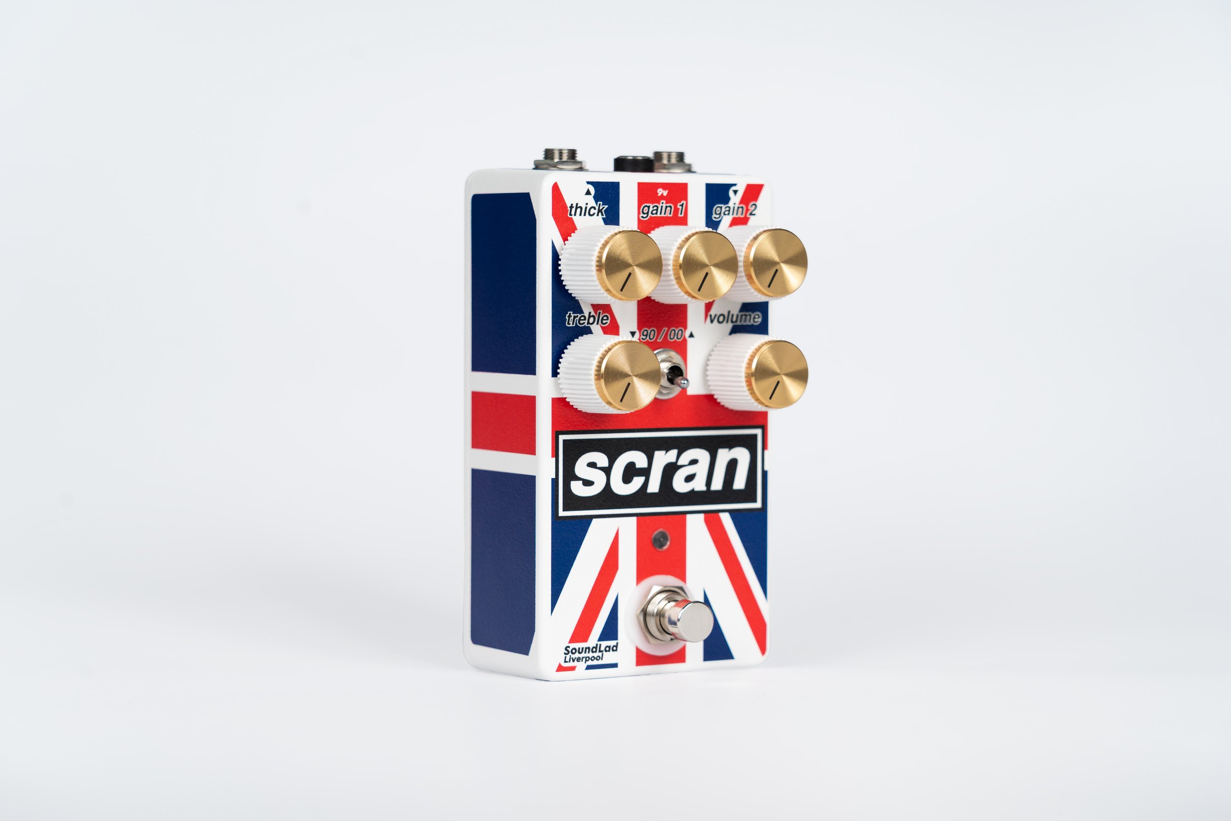 Guitar effects pedal with Union Jack design, labeled 'scran,' featuring multiple gold knobs and switches for tone, gain, treble, volume, and boost.