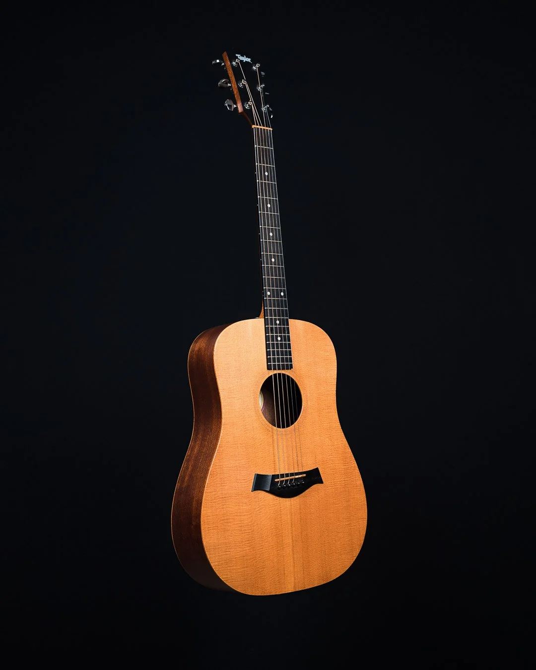 An acoustic guitar with a wooden body and black fretboard against a black background.