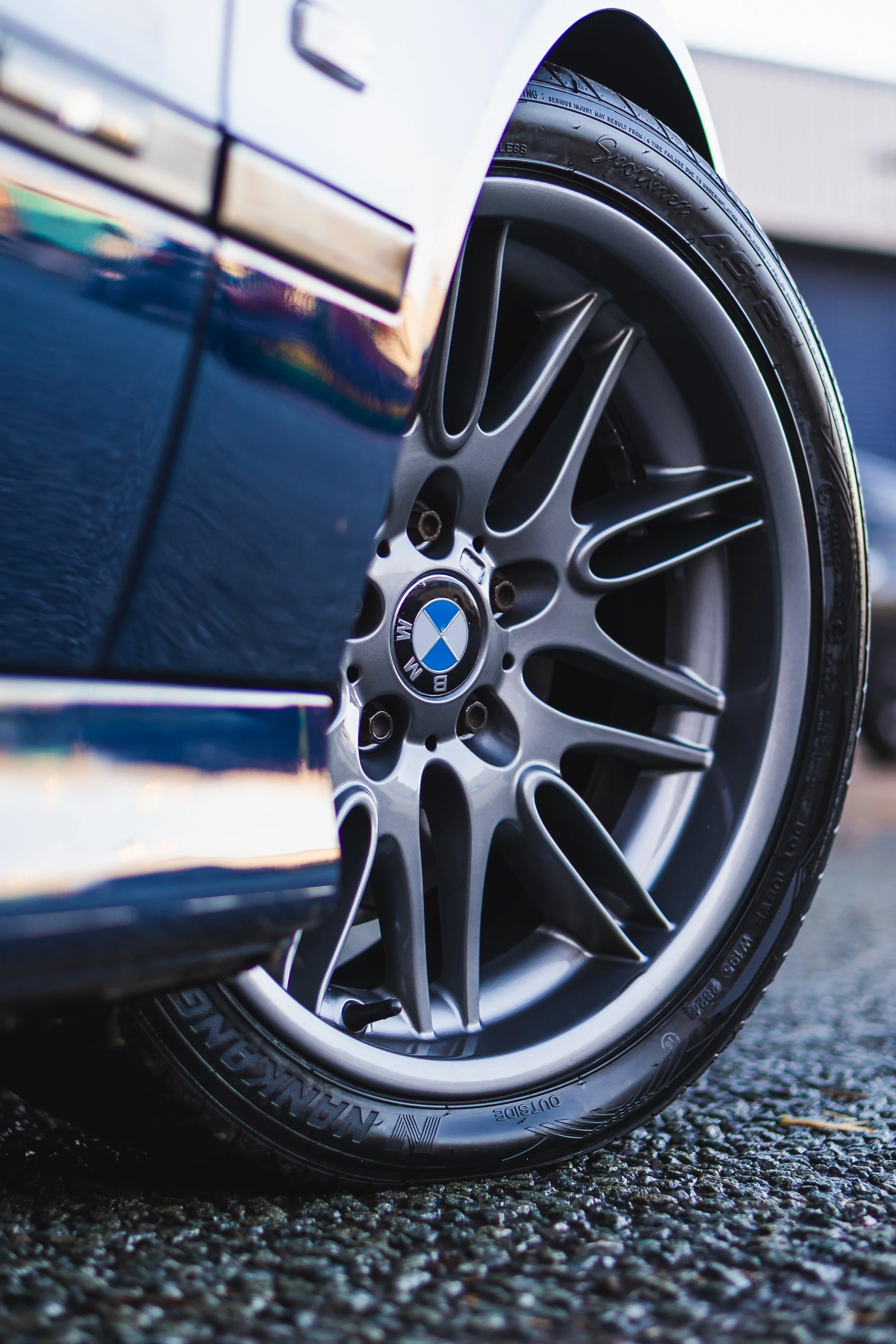 Close-up of a BMW car wheel with a black tire on a textured asphalt surface.