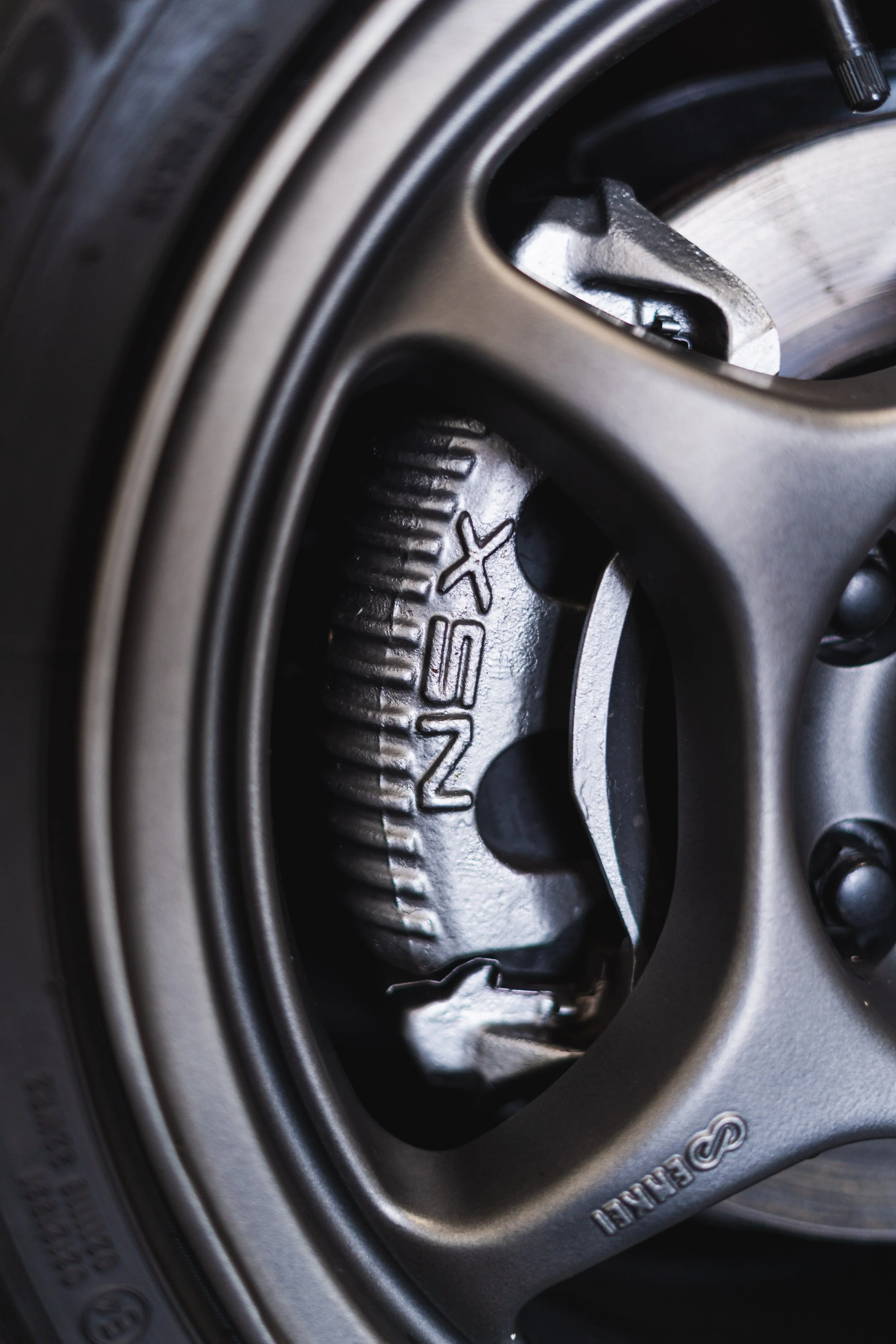 Close-up view of a silver brake caliper with the brand name 'NISSAN' embossed on it, behind a wheel rim on a car.