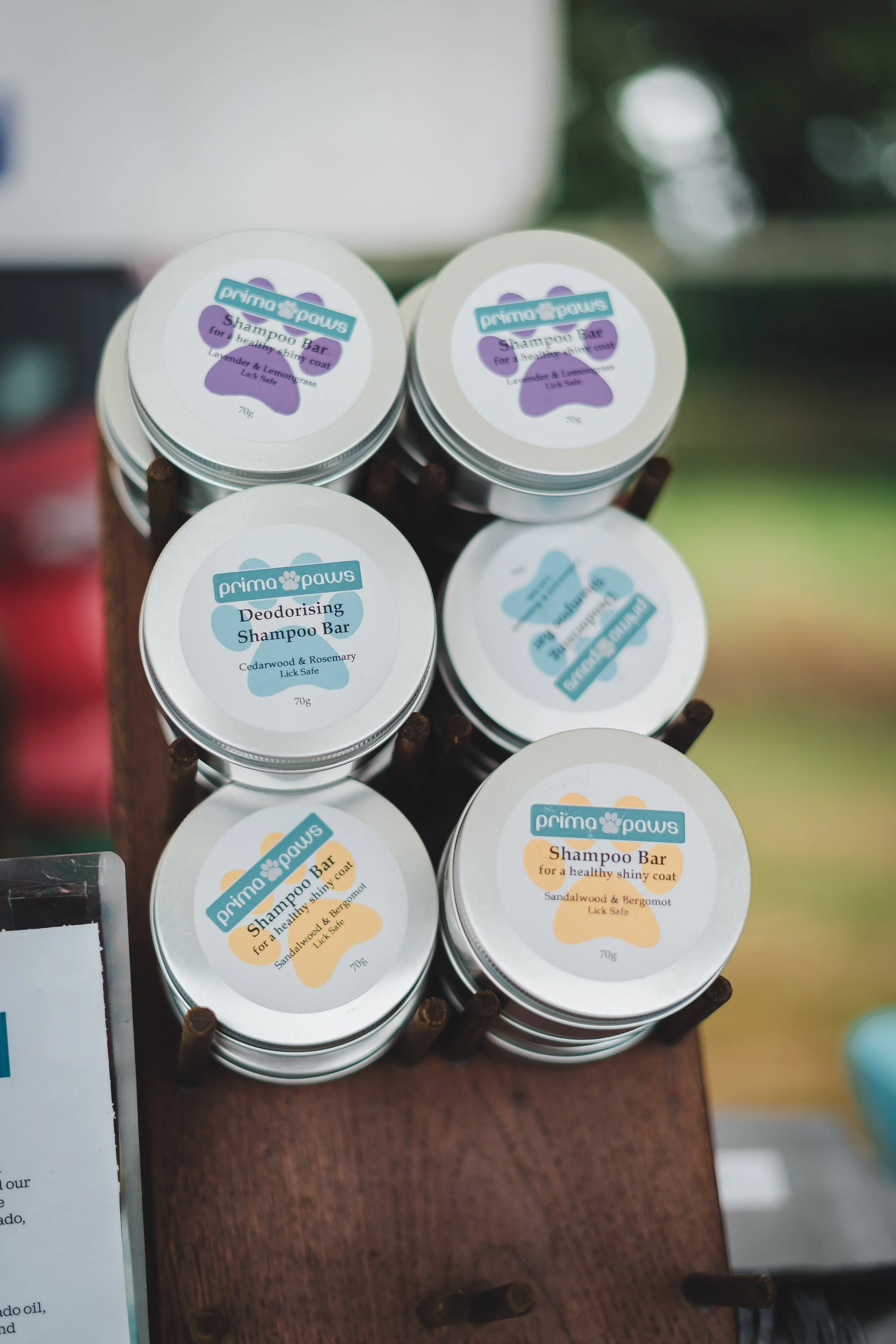 Assorted Prima Paws shampoo and deodorizing soap bars in small circular tins displayed on a wooden stand