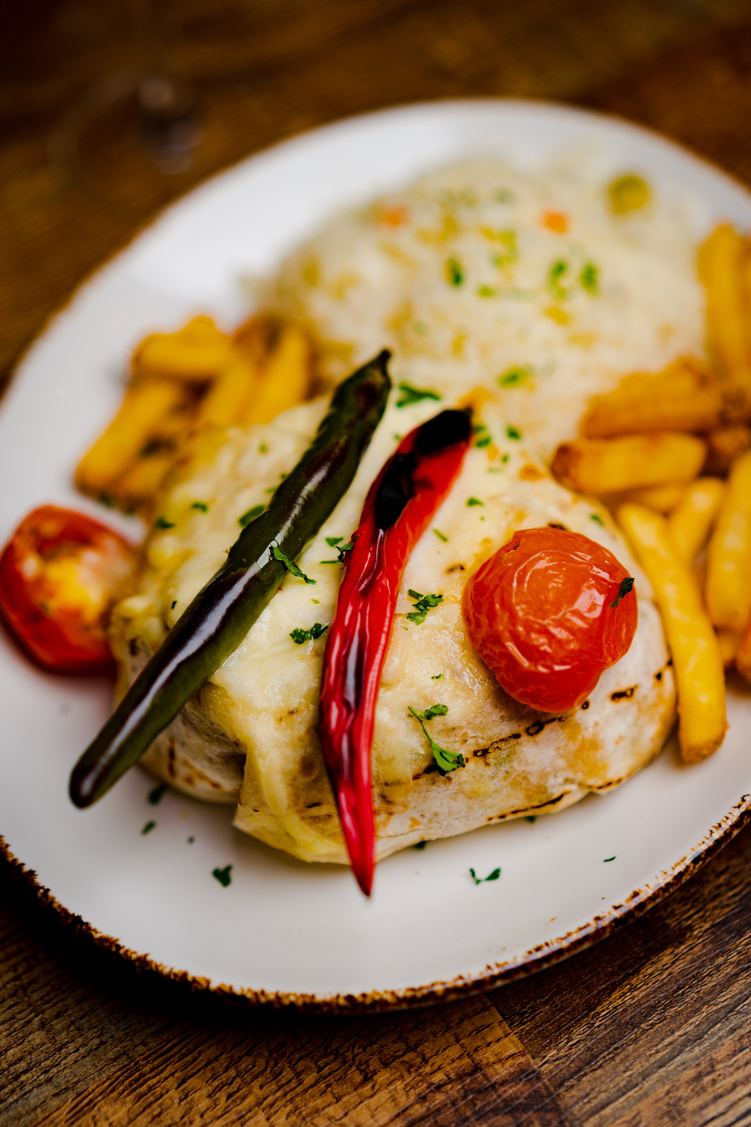 Mexican plate with grilled chicken topped with melted cheese, roasted cherry tomatoes, and grilled peppers, served with rice on a plate.