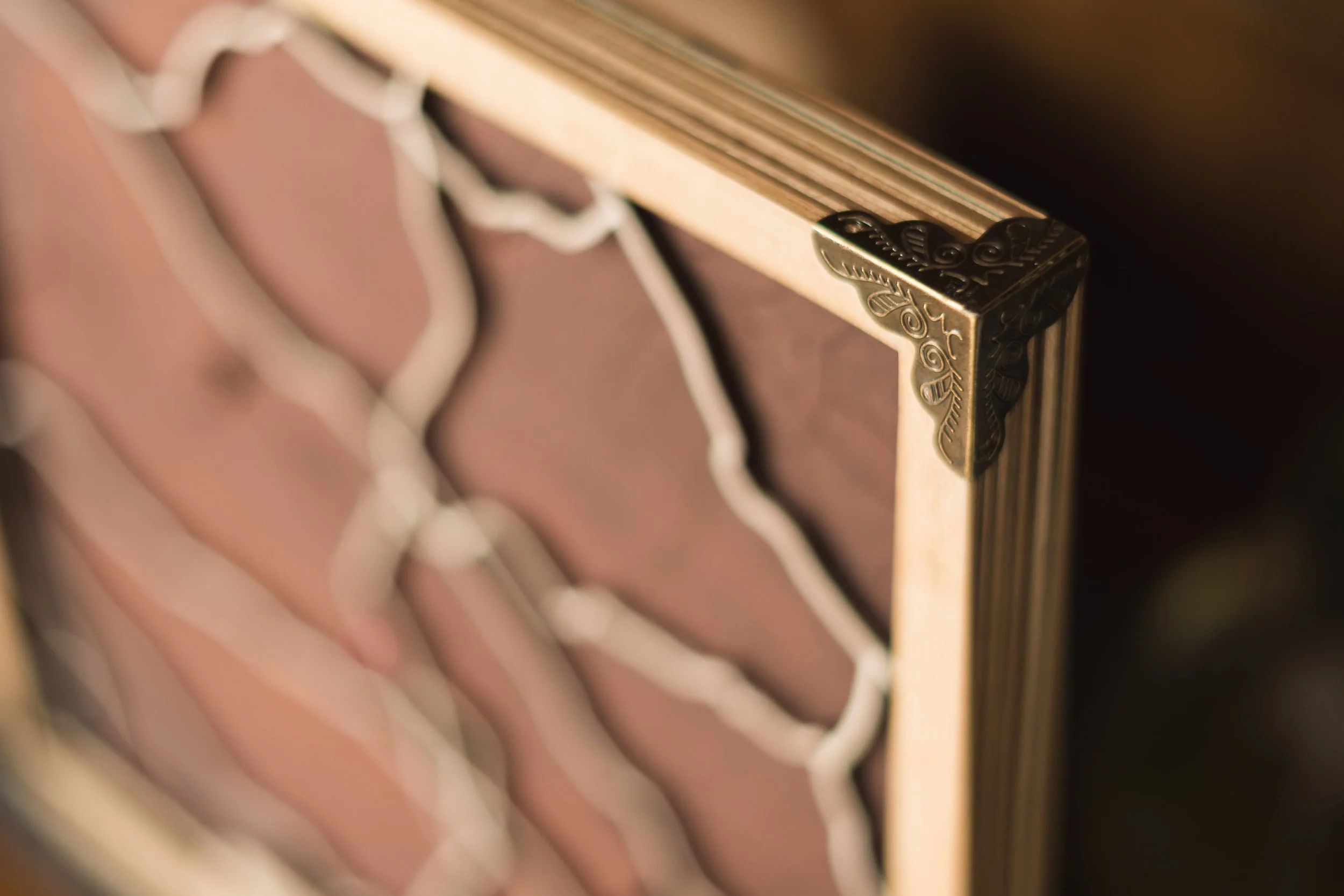 Close-up of a wooden frame with decorative brass corner ornament, showing a latticework detail behind the frame.