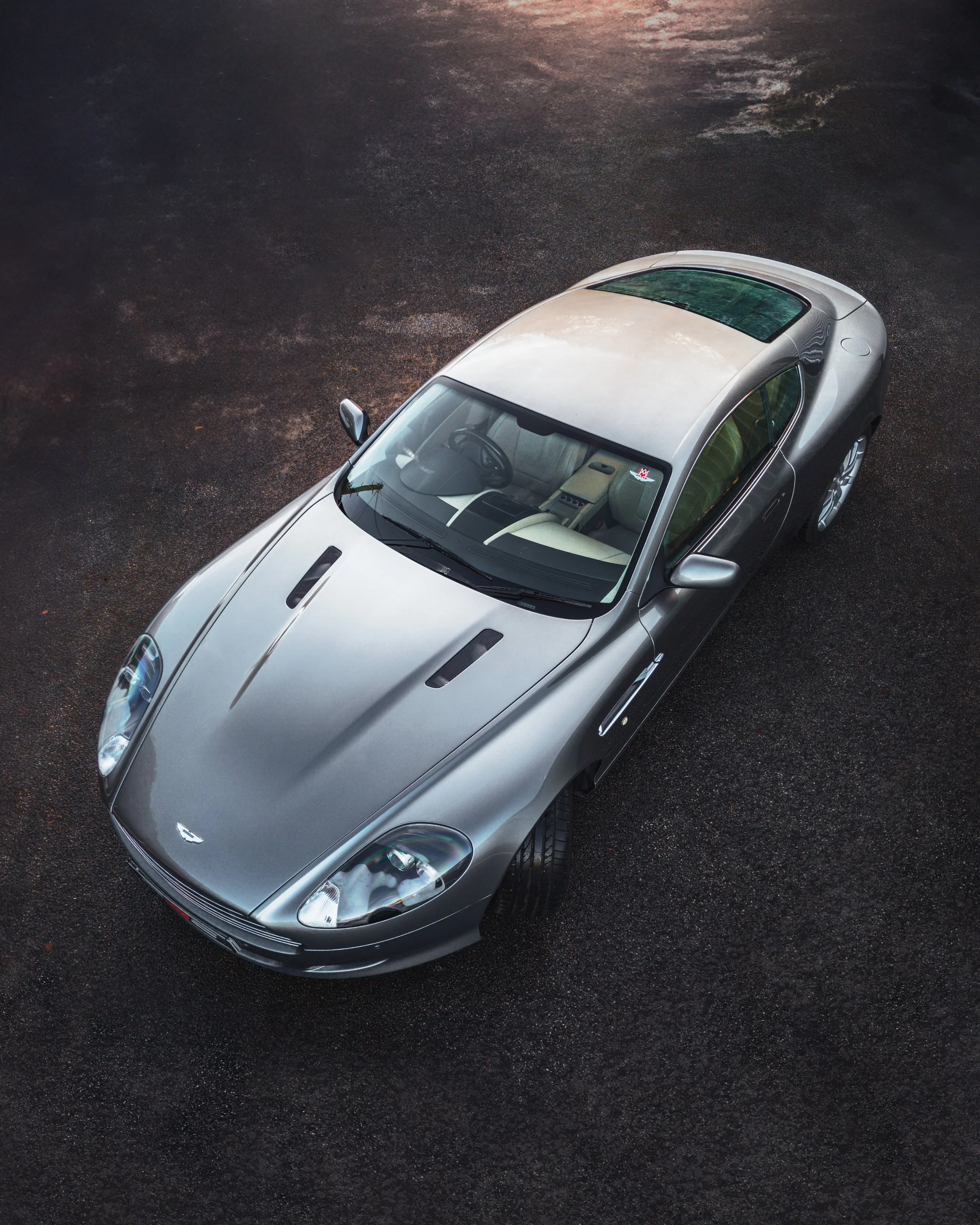 A silver sports car parked on a dark asphalt surface, viewed from an overhead angle.