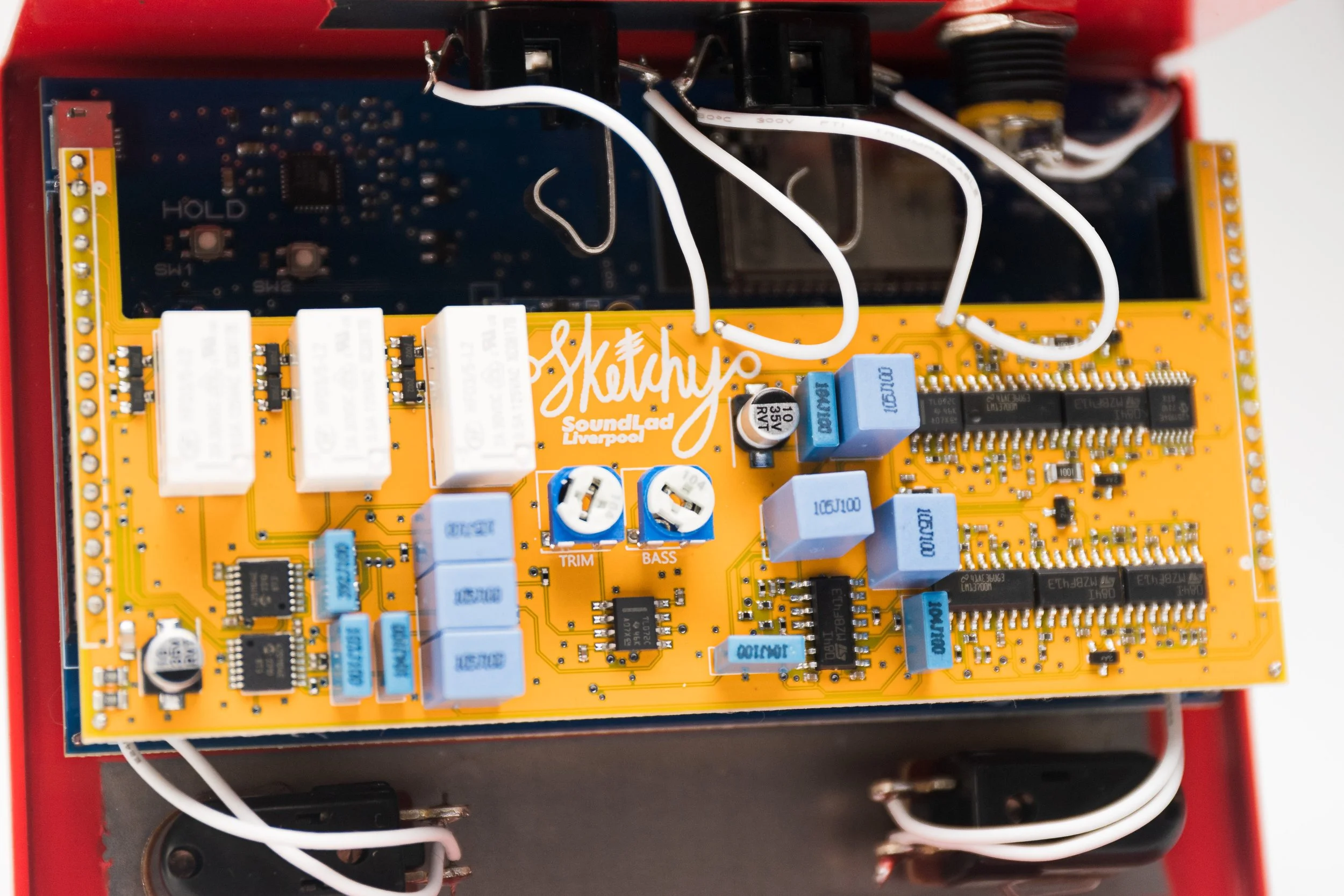 Close-up of an electronic circuit board with various components, including blue and white capacitors, black integrated circuits, and connectors, mounted inside a red enclosure.
