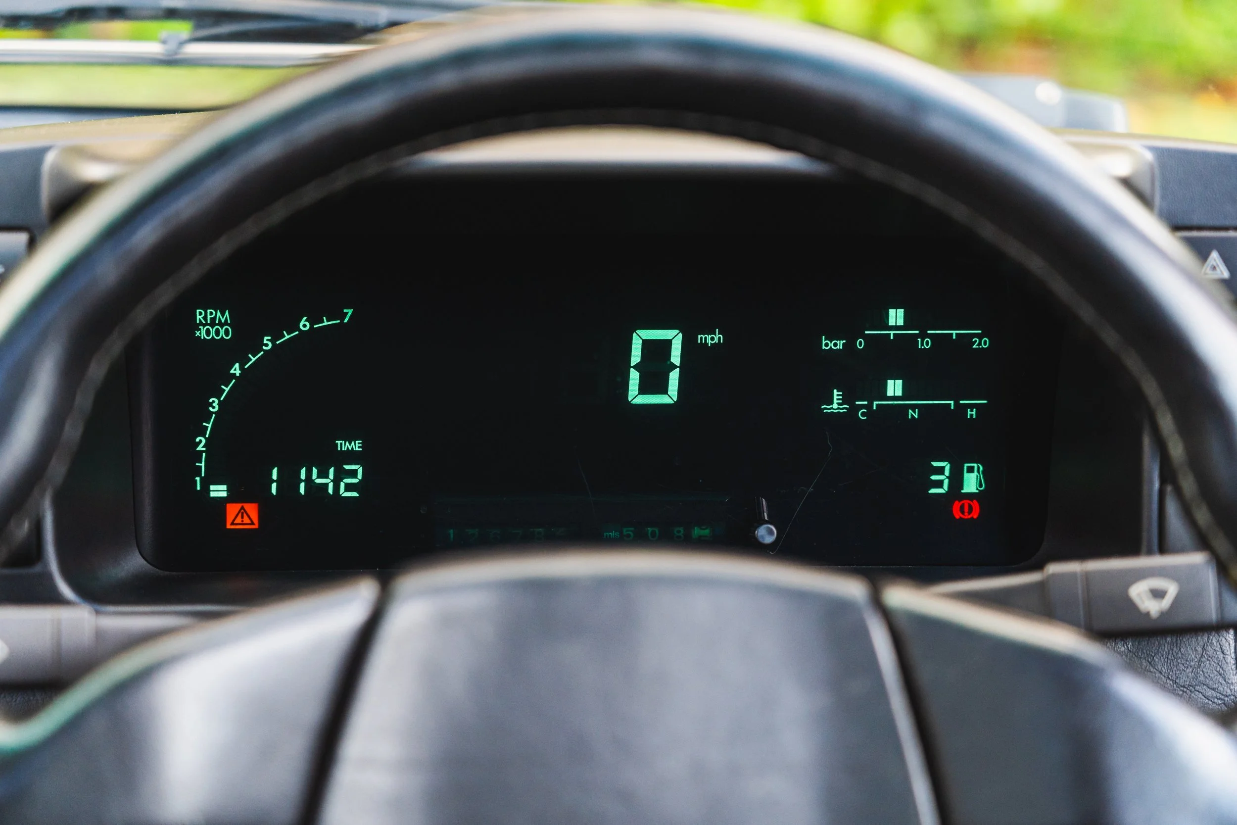 Digital car dashboard showing 0 mph, with warning lights on, including brake warning light and tire pressure warning light. The dashboard also displays the time as 11:42 and the date as 17/07, along with fuel, temperature gauges, and RPM meter.
