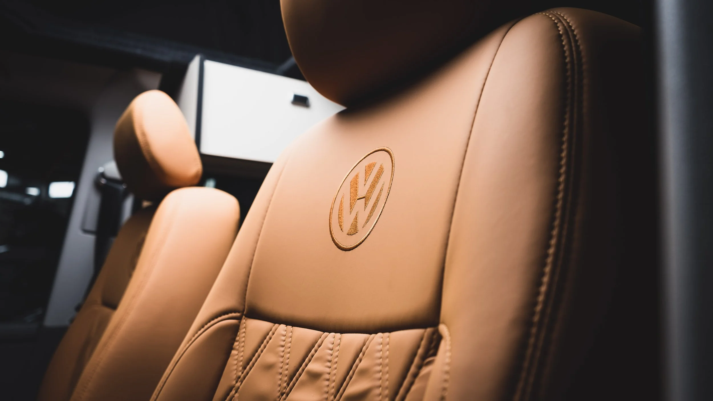 Close-up of beige car seats with the Volkswagen logo embroidered on the headrest in a dimly lit vehicle interior.
