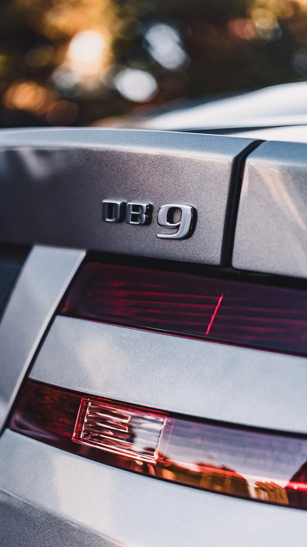 Close-up of the rear end of a silver Mercedes-Benz DB 9 car, showing the tail light and badge.