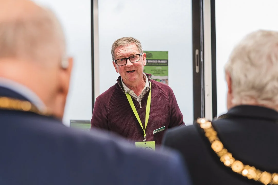 A man wearing glasses and a maroon sweater speaking to two people at an indoor event.