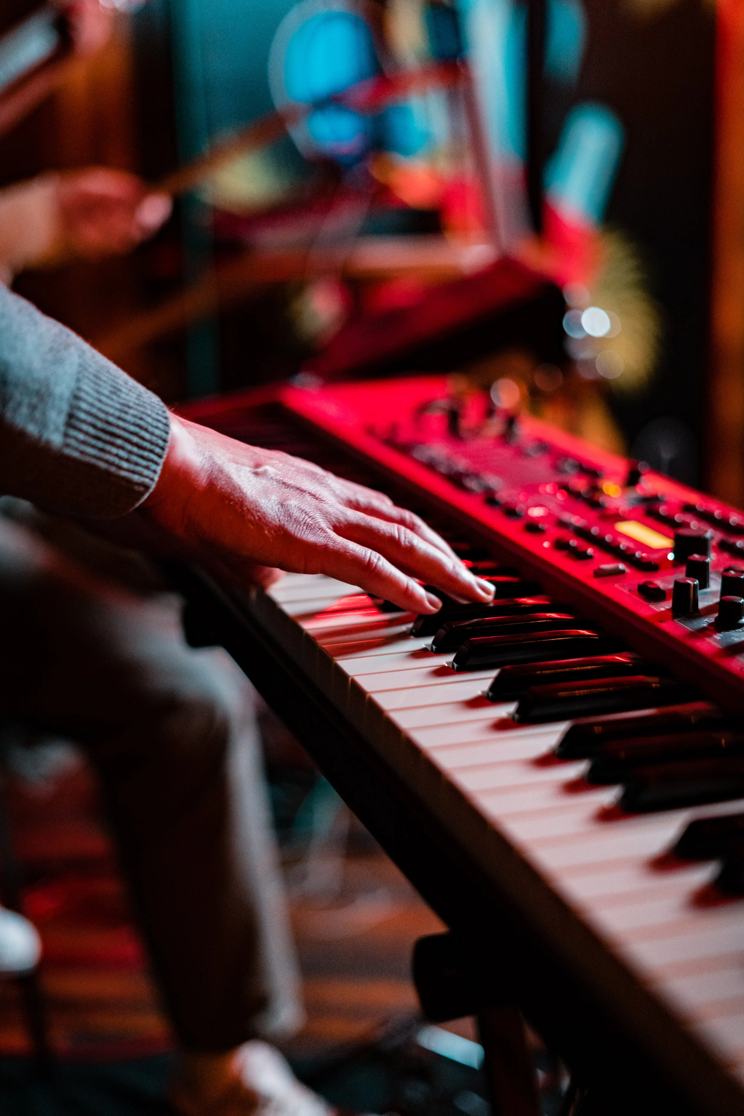 A person playing a keyboard or synthesizer, with their hand on the keys, in a dimly lit setting.
