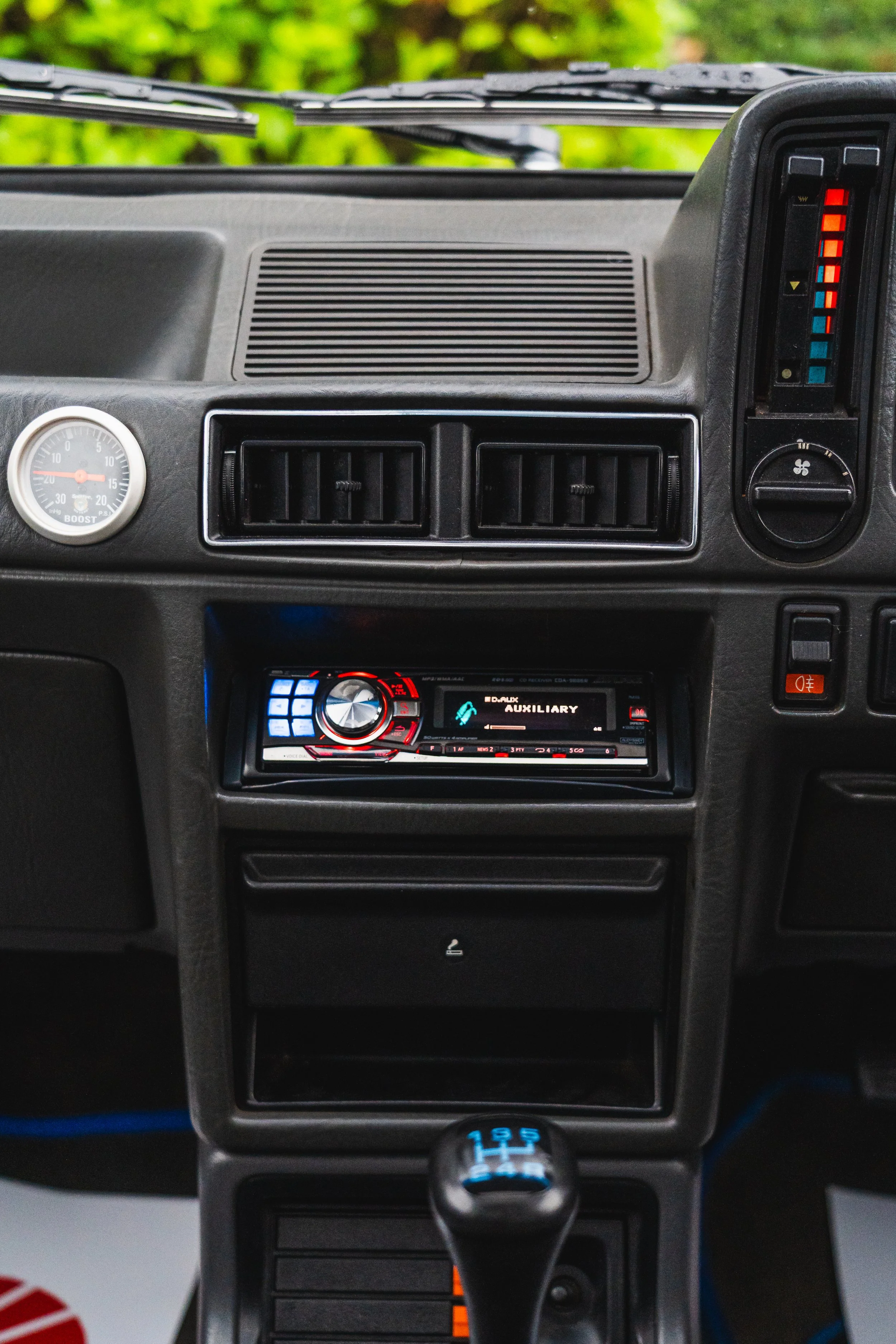 The interior dashboard of a vehicle showing air vents, a boost gauge, a digital display with auxiliary audio, climate controls, and a manual gear shift.