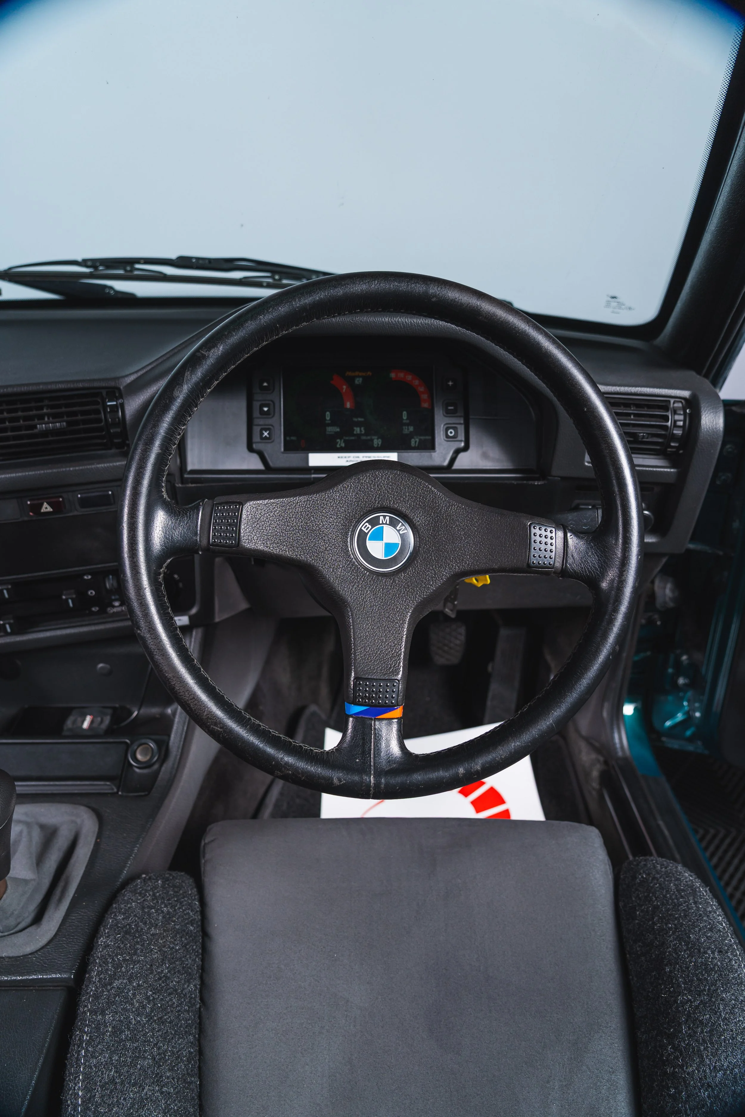 The interior dashboard view of a black BMW vehicle, showing the steering wheel with BMW logo, digital instrument panel, and common car interior features.
