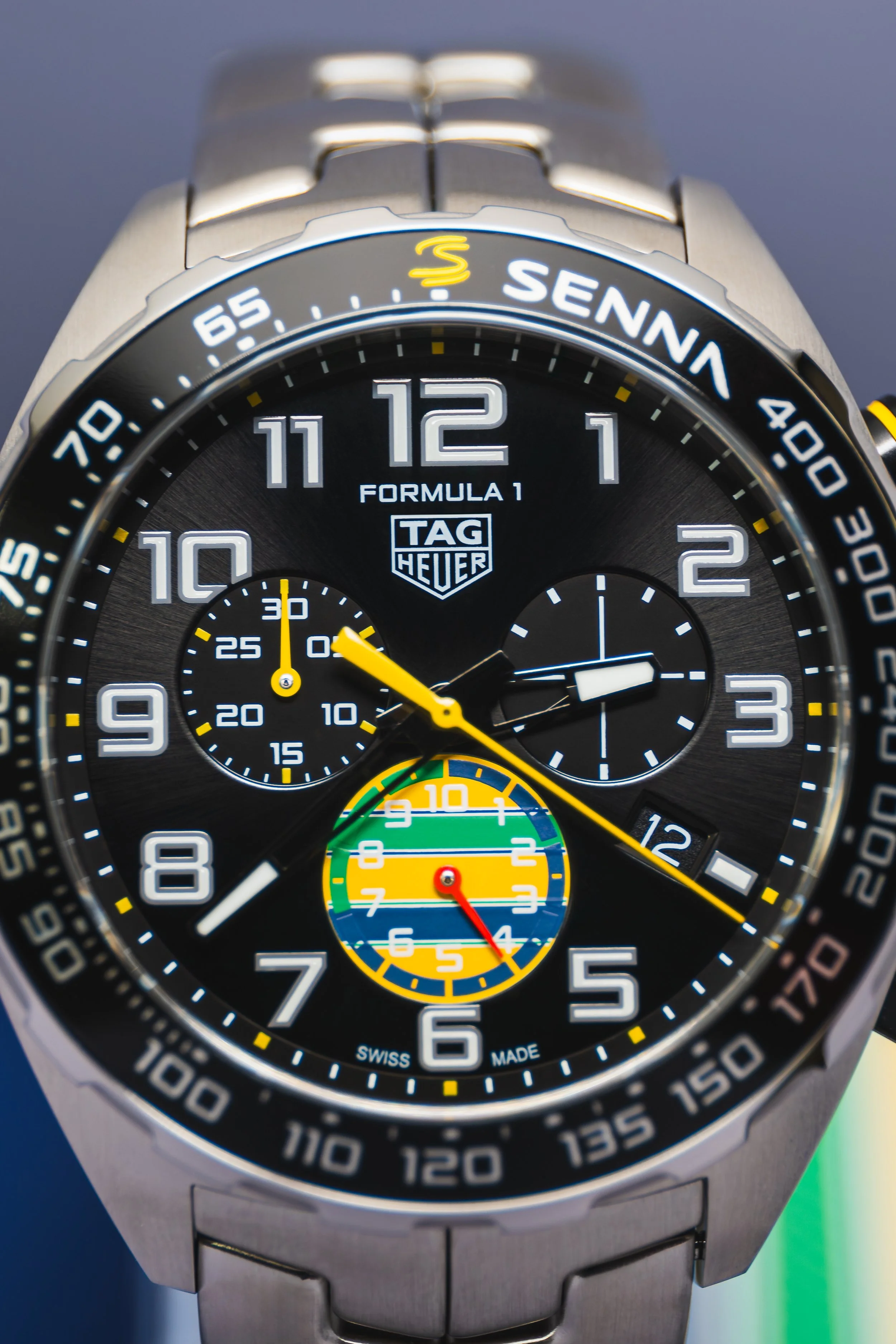 Close-up of a TAG Heuer Formula 1 watch with a black dial, silver case, and a multicolored chronograph face. The bezel features numbering and branding details.