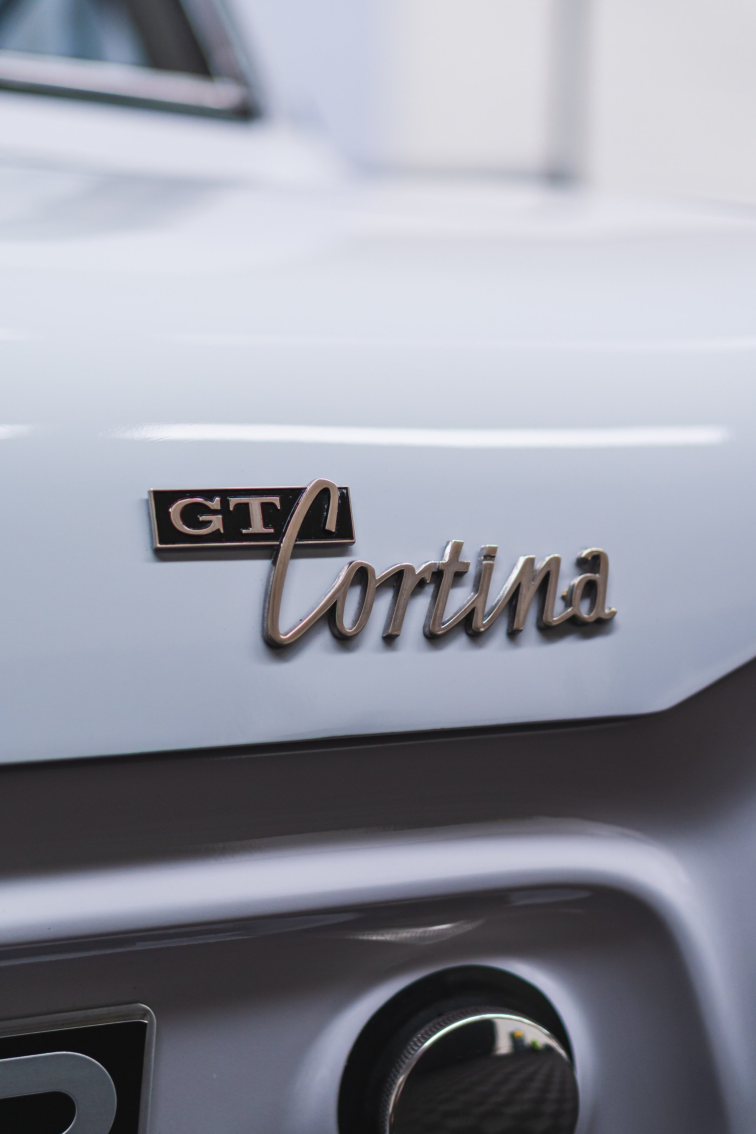 Close-up of a classic white Porsche car badge reading 'GT' and 'Cortina' on the rear.