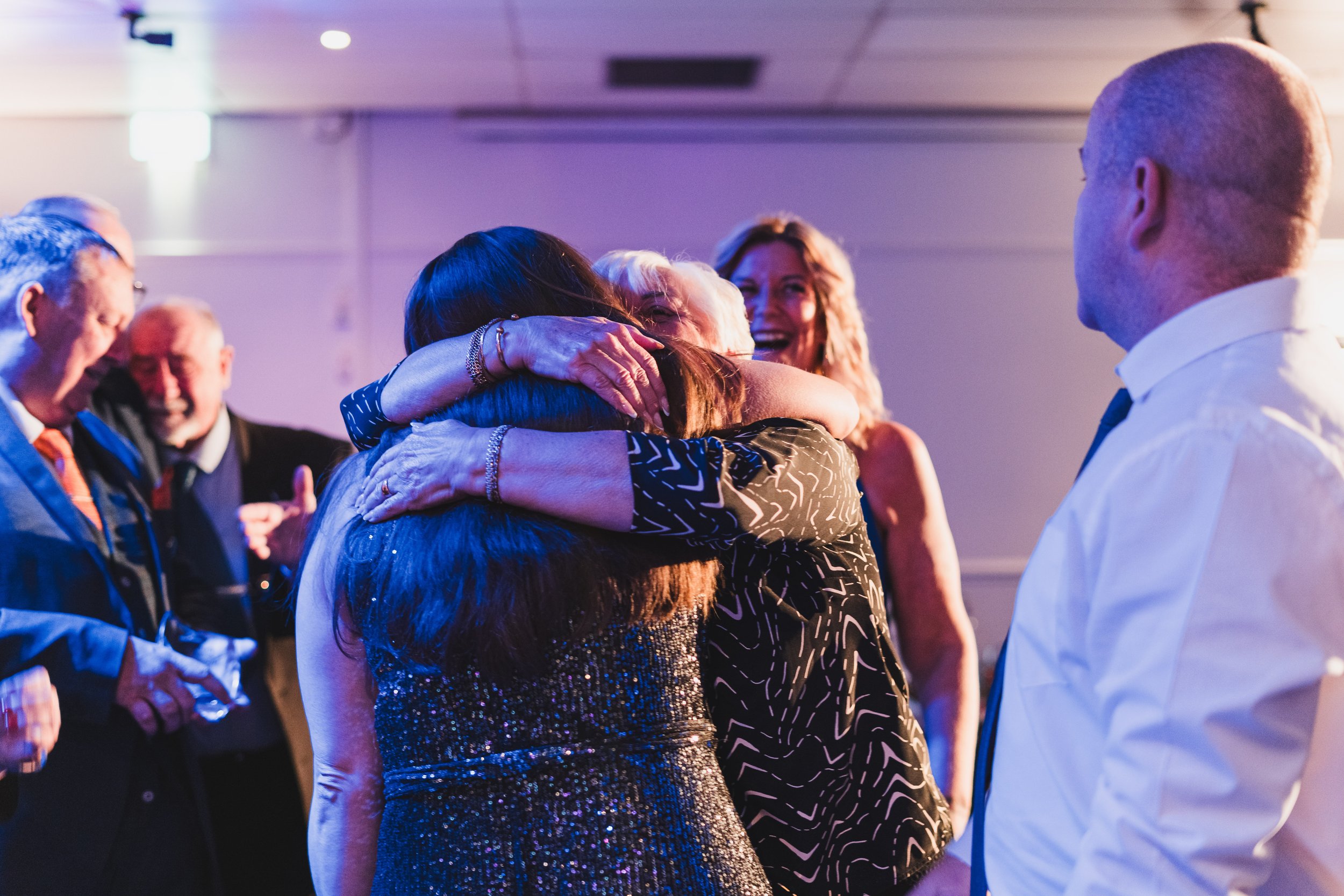 People hugging and celebrating at an event, with smiling faces and formal attire.