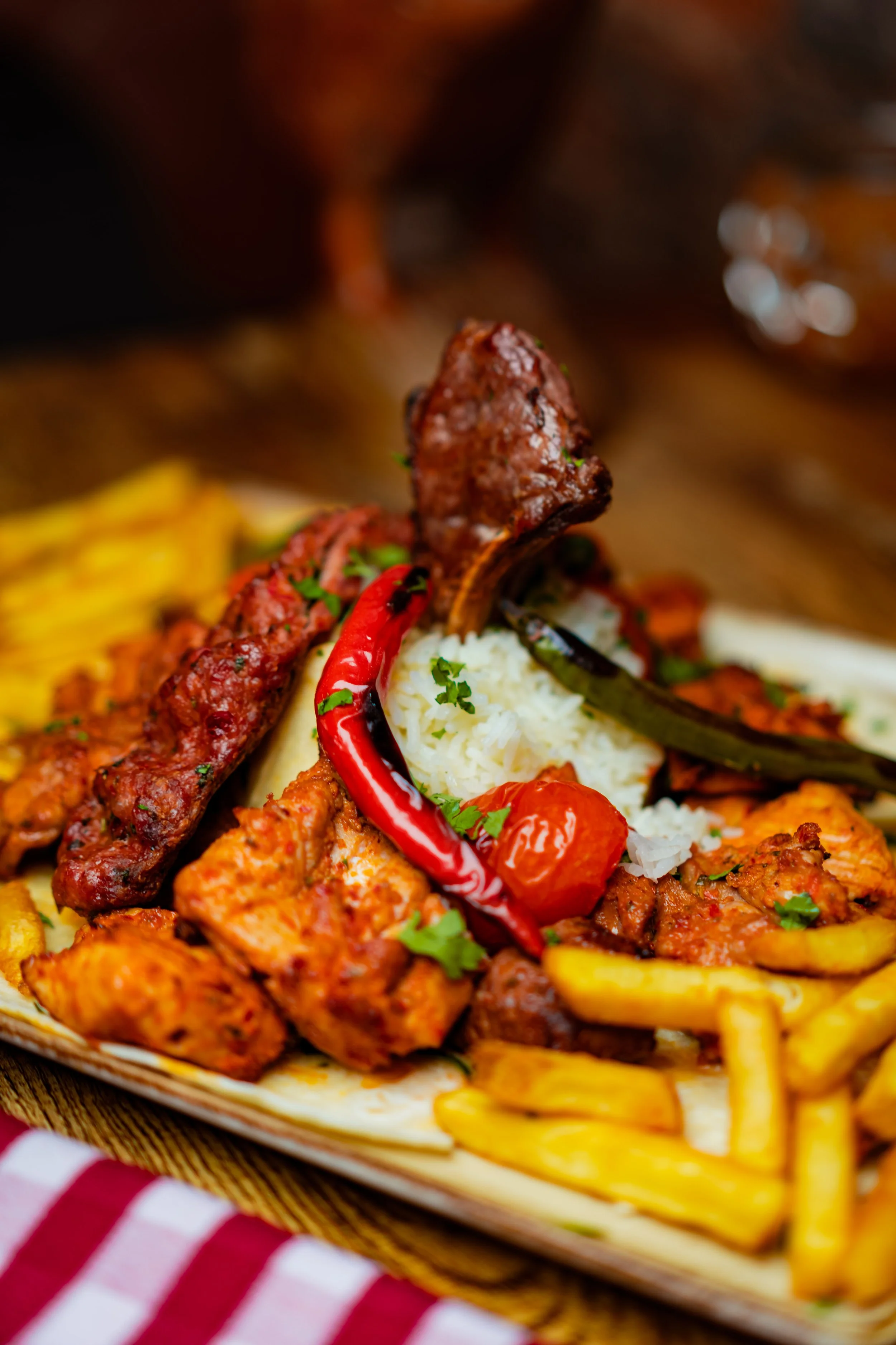 A plate of Middle Eastern or Mediterranean cuisine including rice, grilled meats like kebabs, grilled vegetables, and French fries, garnished with herbs and a red chili pepper.