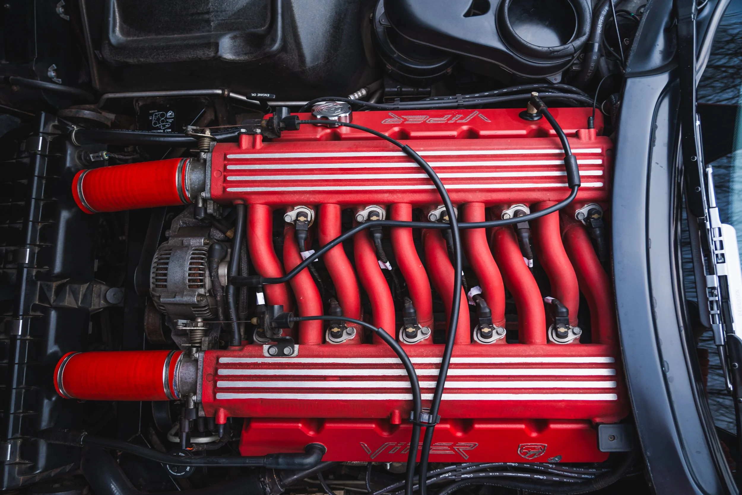 Close-up of a car's engine with a red intake manifold and red ignition wires, with black hoses and metal components visible.