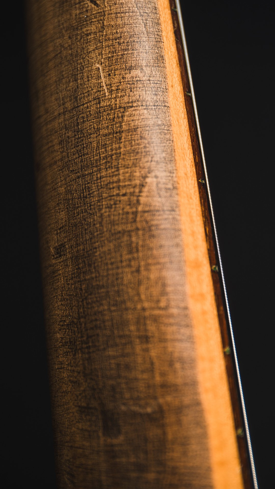 Close-up of a wooden musical instrument, likely a guitar neck or fretboard, with visible strings and frets.