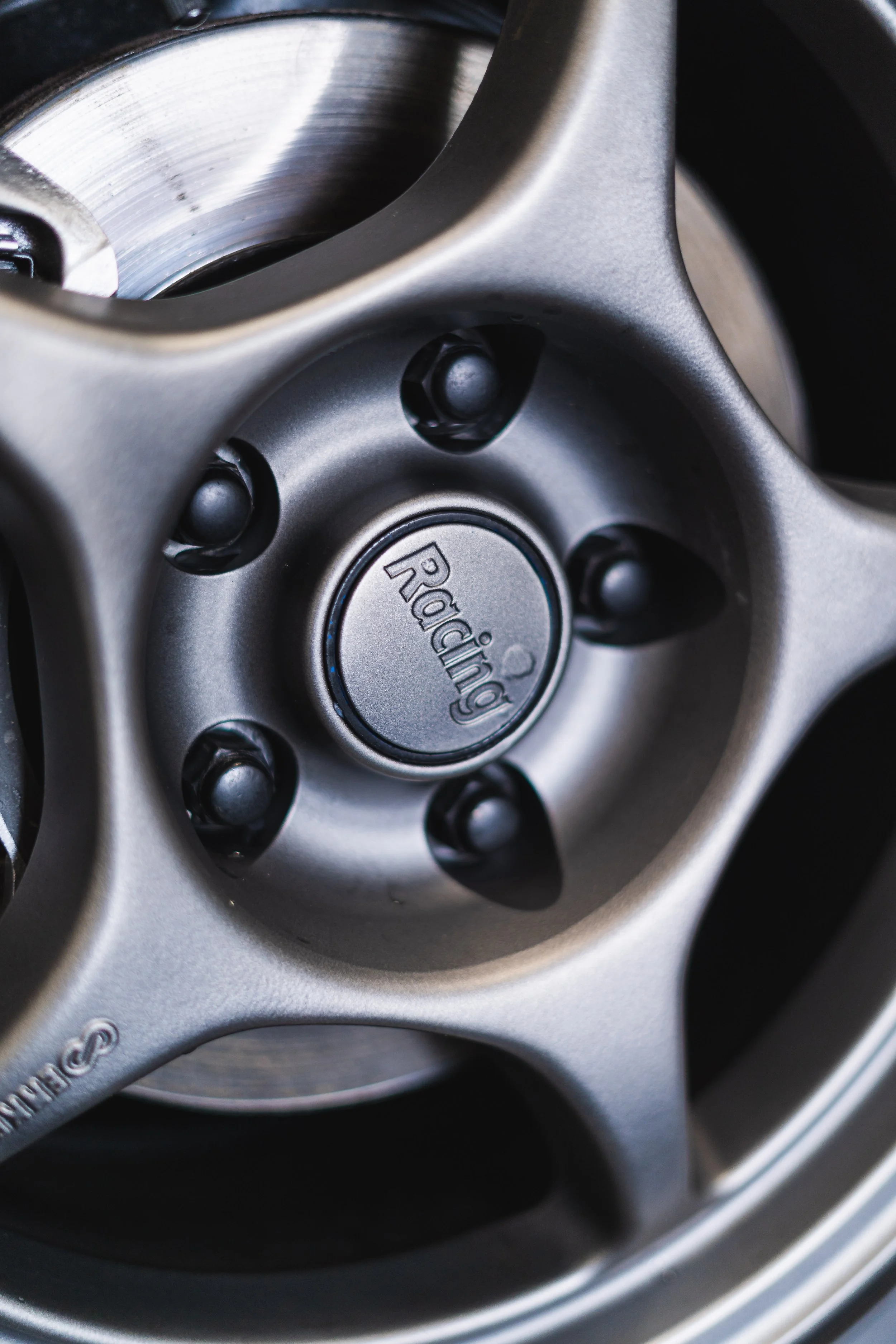 Close-up of a racing-style car wheel with a silver metallic finish, showing the center cap labeled 'Racing' and five lug nuts.