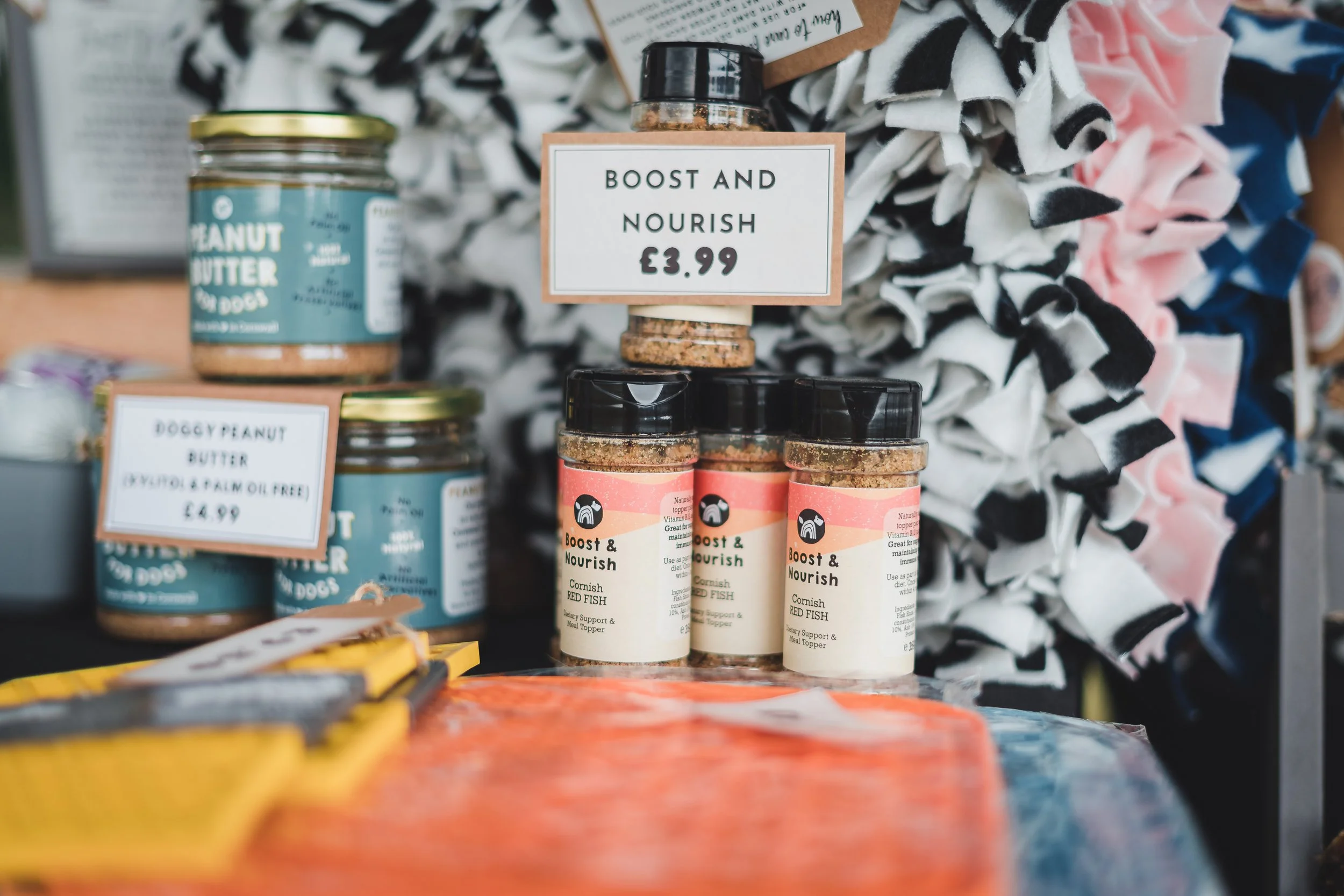 Display of dog food and peanut butter jars on a table at a pet store, with a sign advertising 'Boost and Nourish' fish food priced at £3.99.