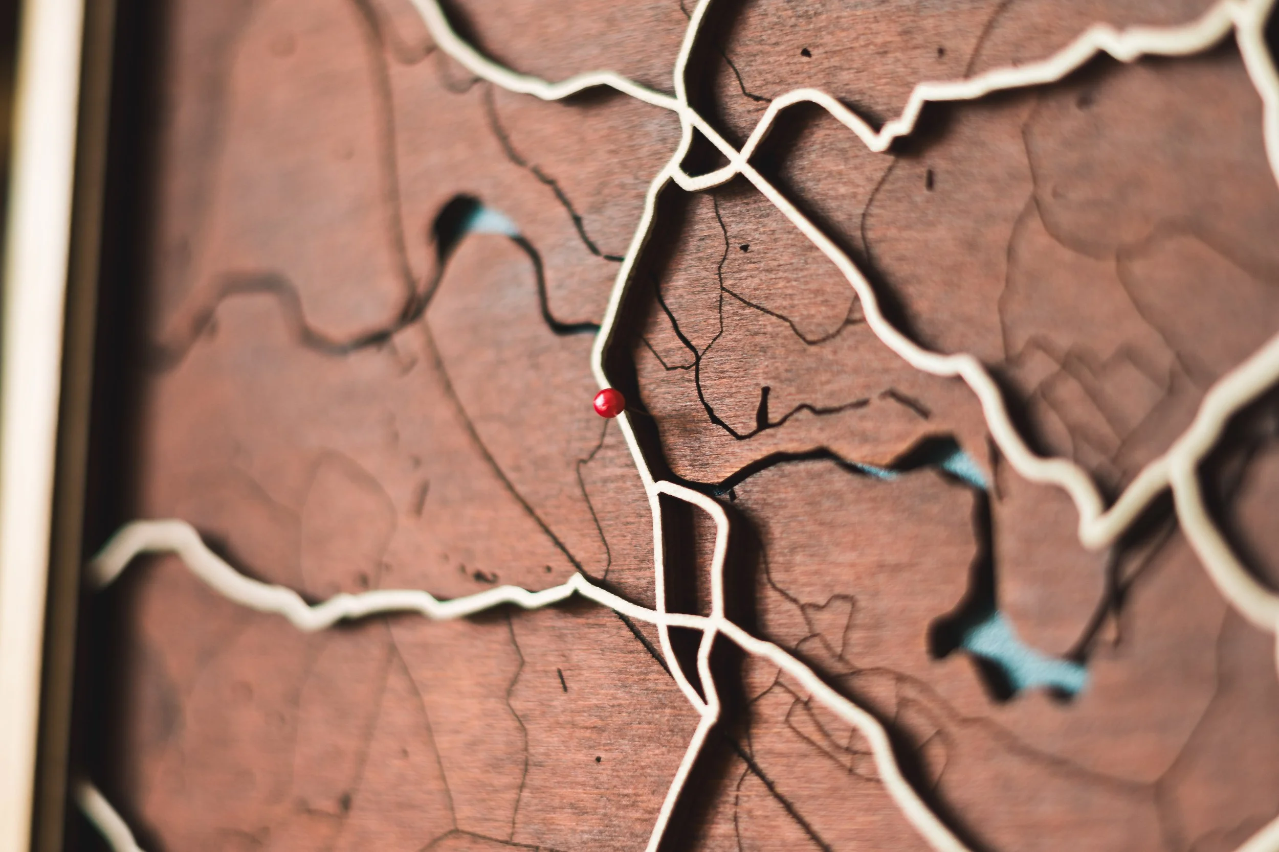Close-up of a wooden map with white borders and a red pin marking a location.